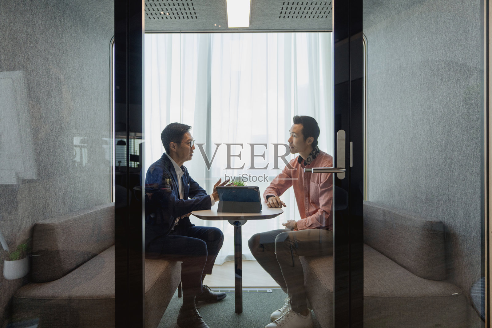 在办公室的隔音舱内，两位亚洲男性同事进行私人商务讨论。照片摄影图片