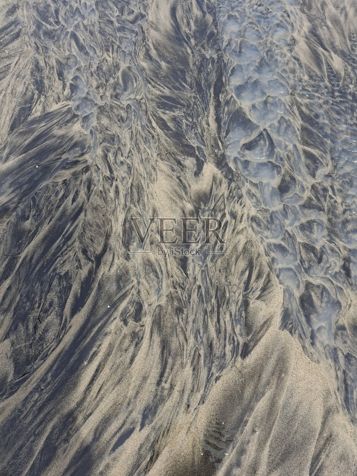 沙滩上湿润沙子的有趣深浅纹理图案，画面展示了海滩上湿沙因水流形成的波浪状纹理和沉积图案。照片摄影图片
