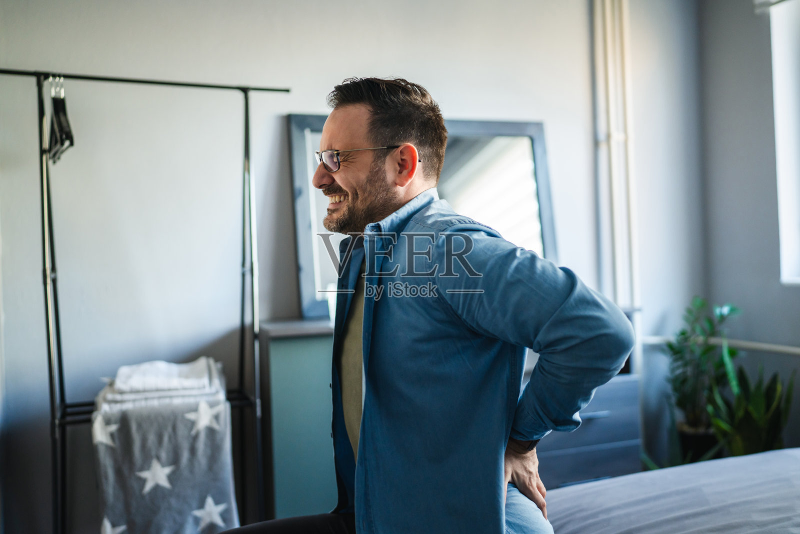 男人在卧室里因腰痛而痛苦地皱眉照片摄影图片