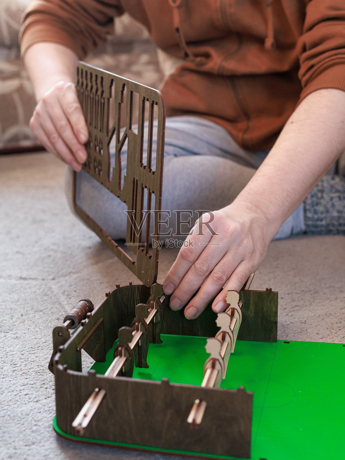 成年男子正在安装复古桌面足球游戏的木质墙壁组件。概念是工艺、怀旧游戏、创作过程、成人娱乐。照片摄影图片