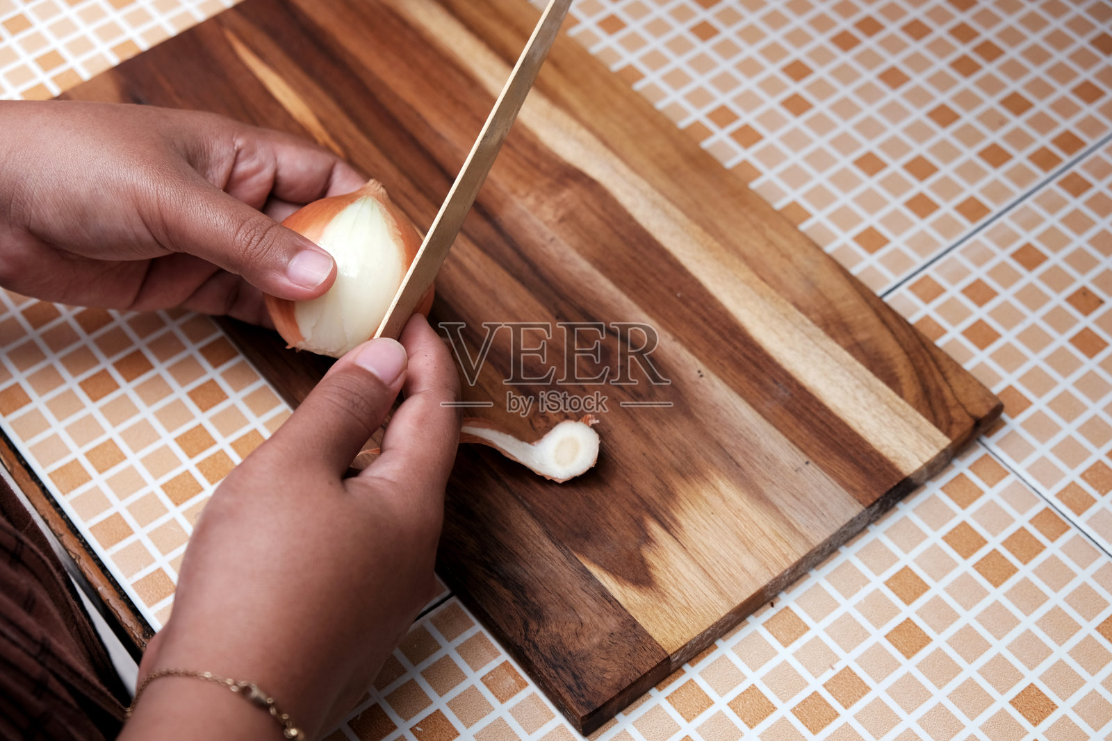 一个女人在厨房里用刀削生洋葱的皮。照片摄影图片