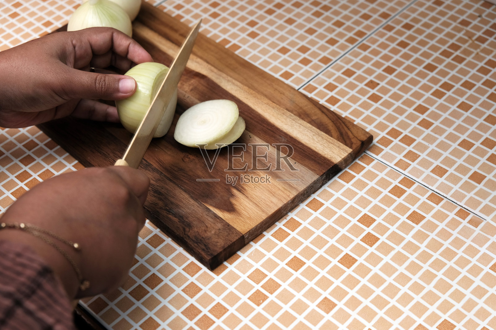 一位女士在厨房的木质砧板上用刀切生洋葱。照片摄影图片