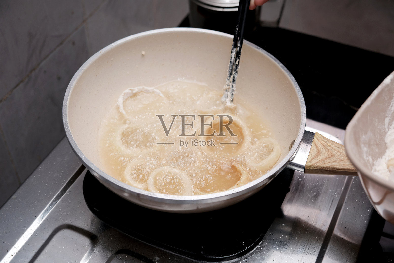 一个人在厨房的热锅里倒入洋葱，制作自制洋葱圈。照片摄影图片