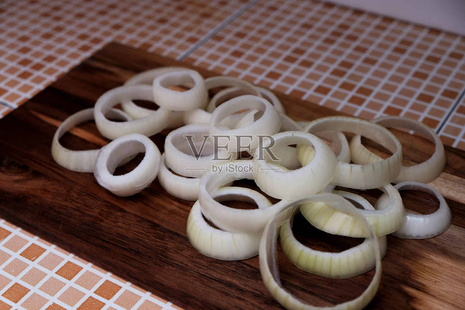 木板上放着一堆切好的生洋葱圈。照片摄影图片