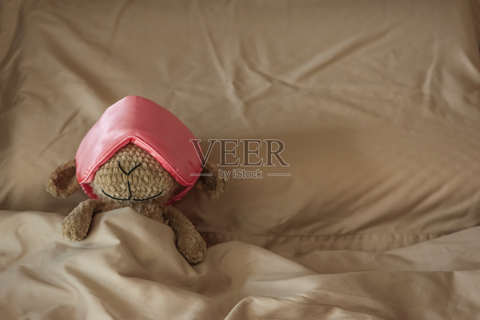 毛绒玩具绵羊戴着丝绸眼罩在舒适的床上睡觉照片摄影图片