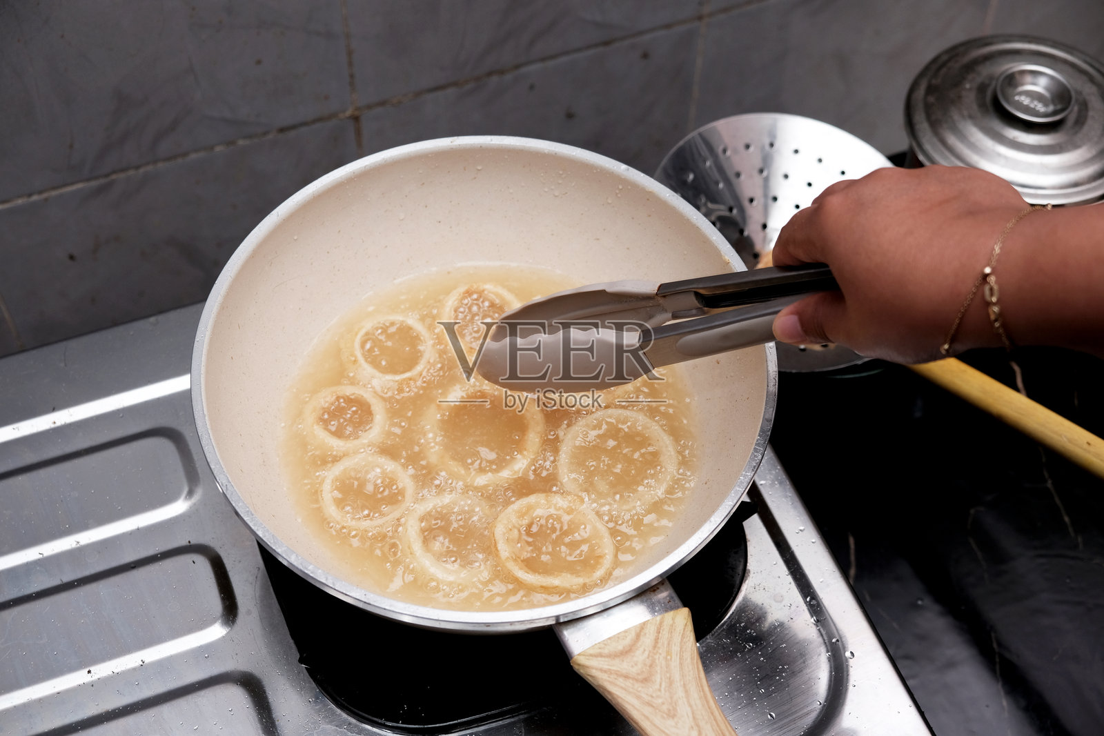 一个人在厨房里用煎炸钳在热煎锅里搅拌洋葱，制作自制洋葱圈。照片摄影图片