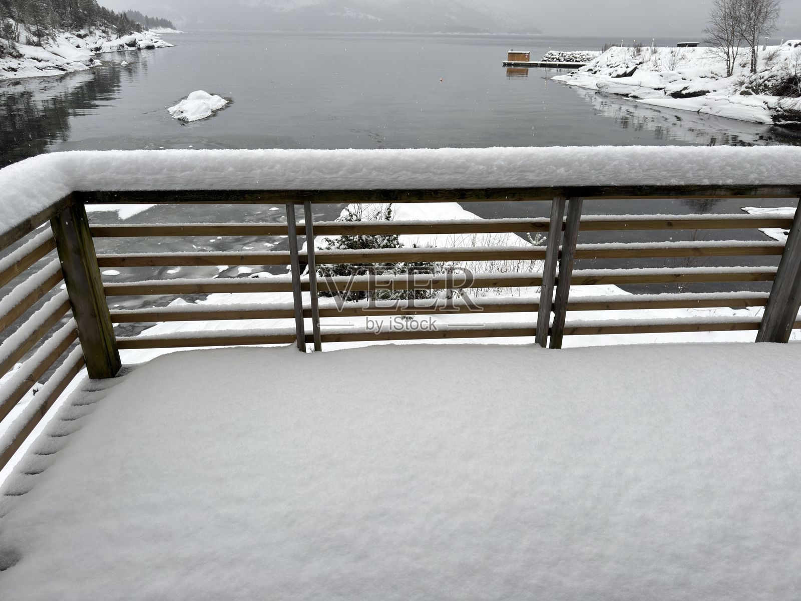 阳台，地板和栏杆上覆盖着雪，俯瞰峡湾和山脉照片摄影图片
