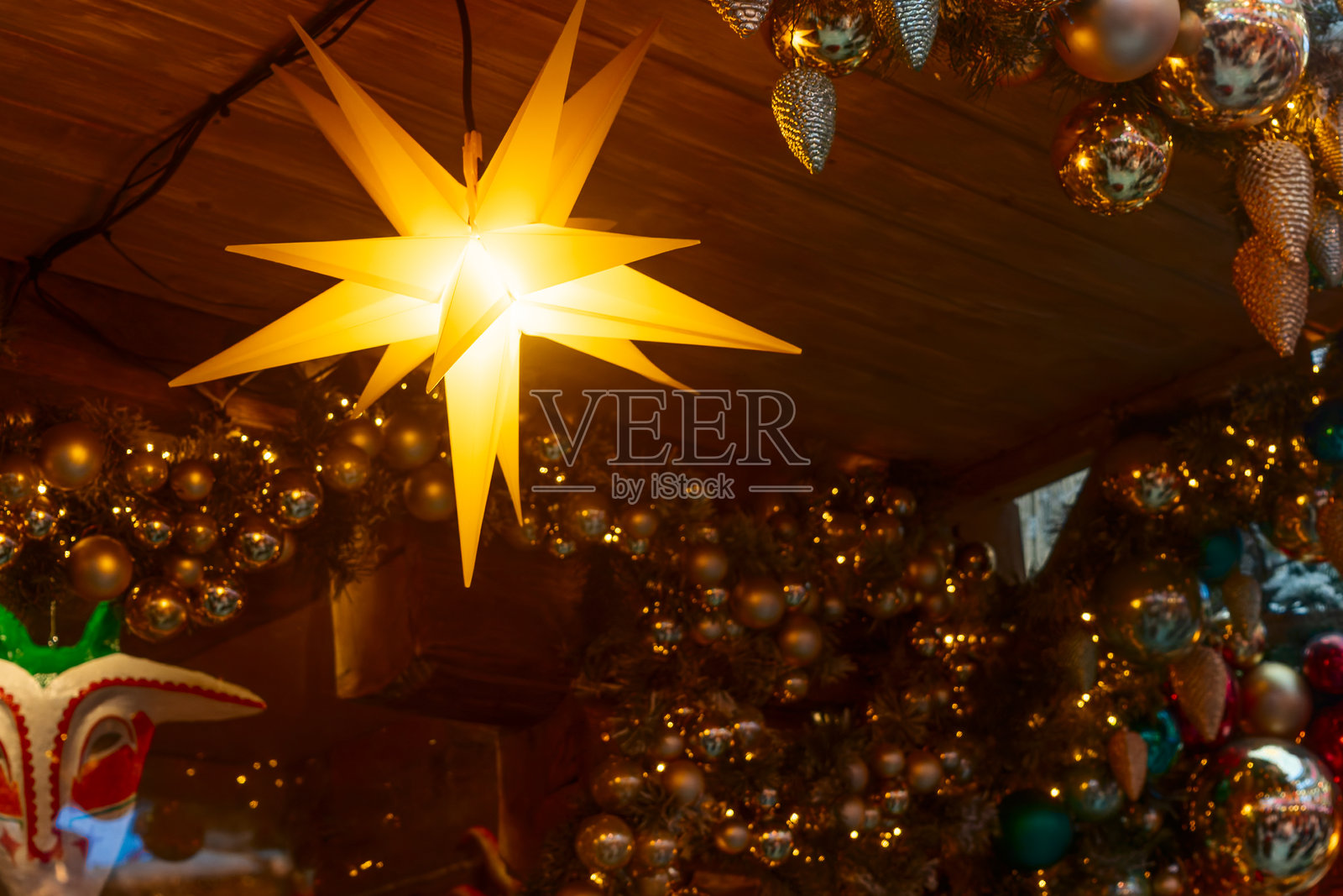 发光的黄色星星装饰品和带有浆果和饰球的节日花环。在舒适的乡村室内，闪耀的星形装饰品搭配节日花环和多彩的饰物。照片摄影图片