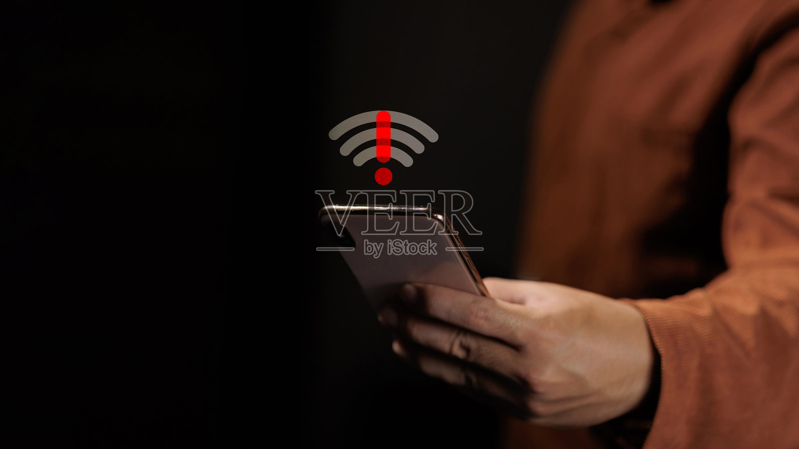 一个人拿着智能手机，上面显示着断开的Wi-Fi信号和红色警报图标。照片摄影图片