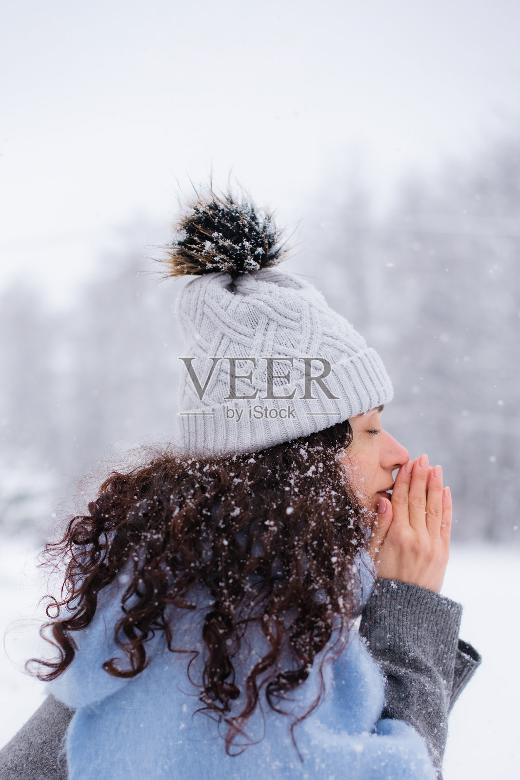 一位女士在雪地公园背景下，对着手心哈气暖着冻僵的手指照片摄影图片