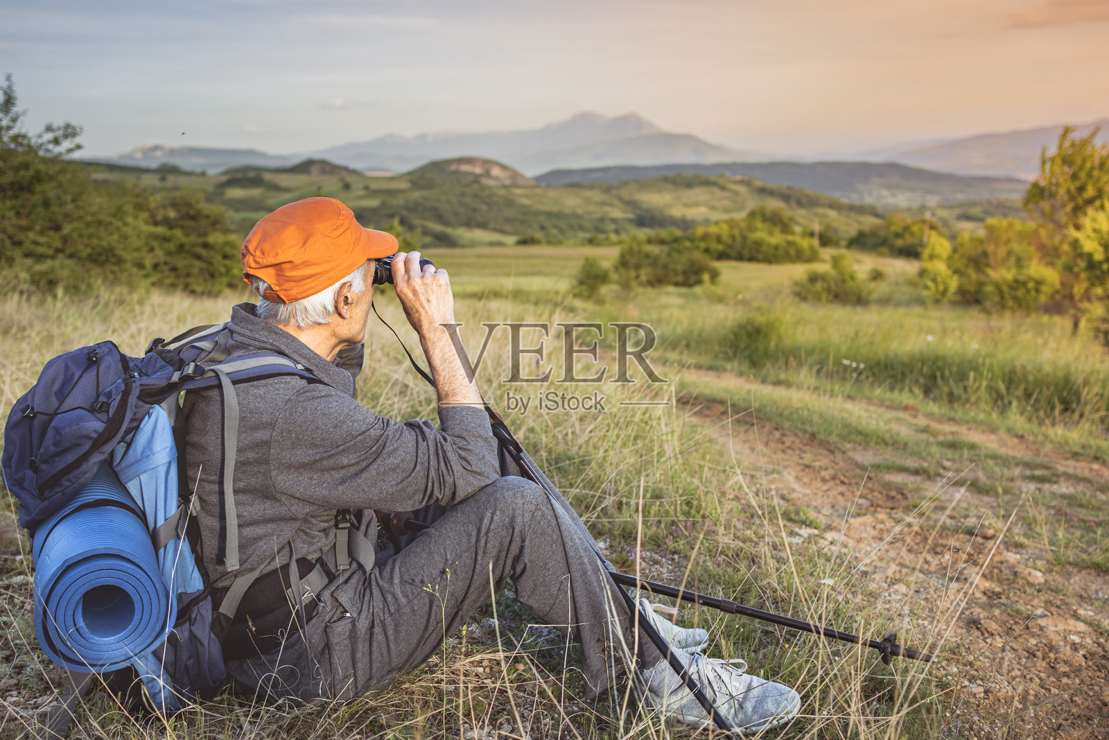 一位背着背包的老年观鸟者，正享受着他的退休生活，徒步穿越大自然，使用登山杖和望远镜寻找稀有鸟类。照片摄影图片