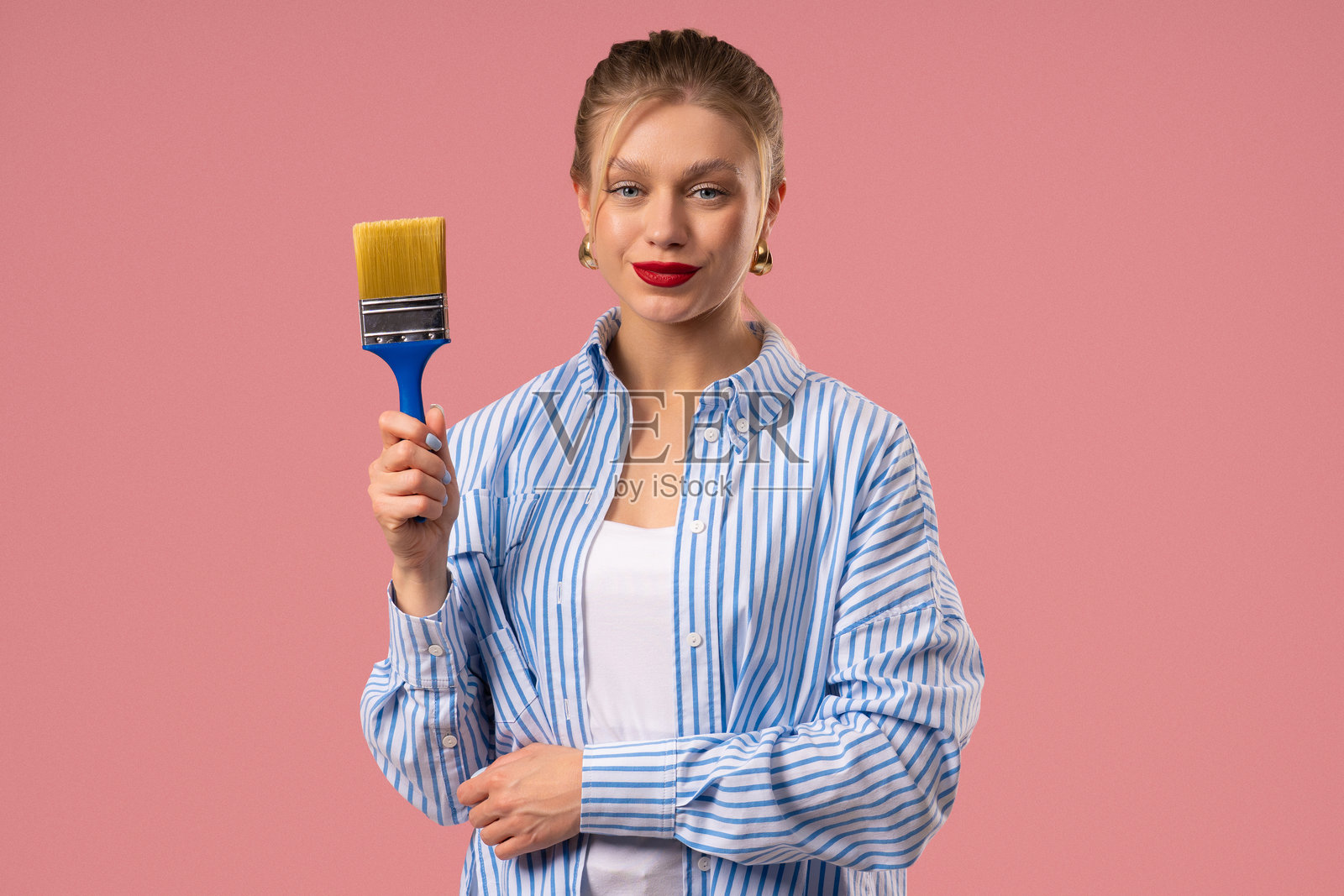 漂亮的微笑女艺术家用画笔在粉色背景上绘画，富有创造力照片摄影图片