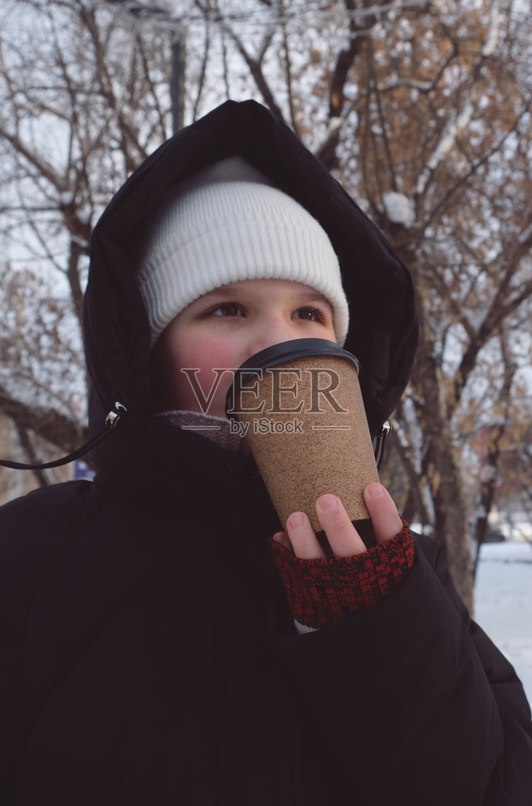 一位穿着暖和冬衣的少女，手持一个外带纸质咖啡杯。这是一个下雪的寒冷早晨，香浓的咖啡让早晨感觉温暖而舒适。杯子上有留白区域可供写字。照片摄影图片