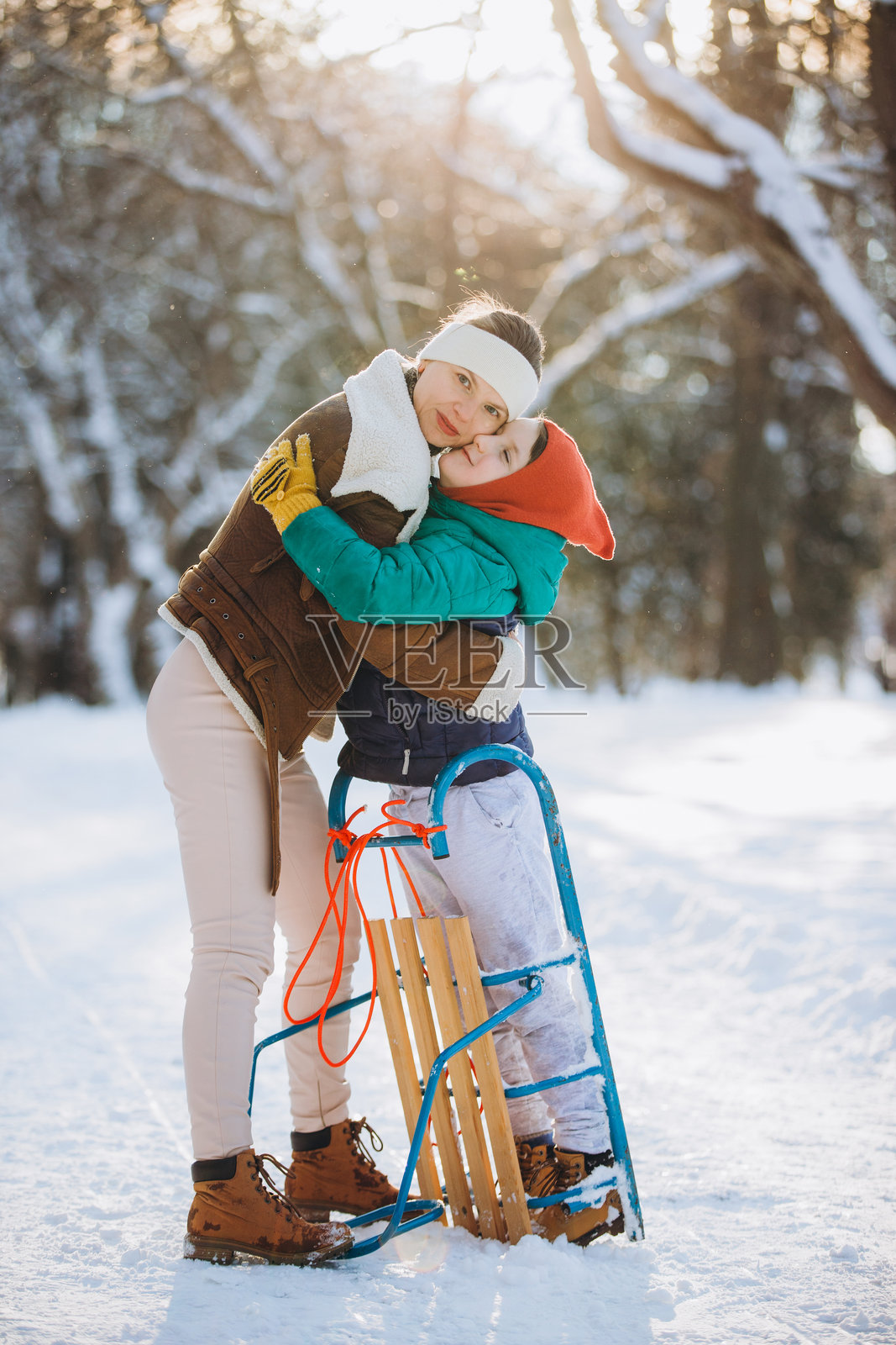 冬天在雪地公园里，一位母亲拥抱着她的儿子照片摄影图片