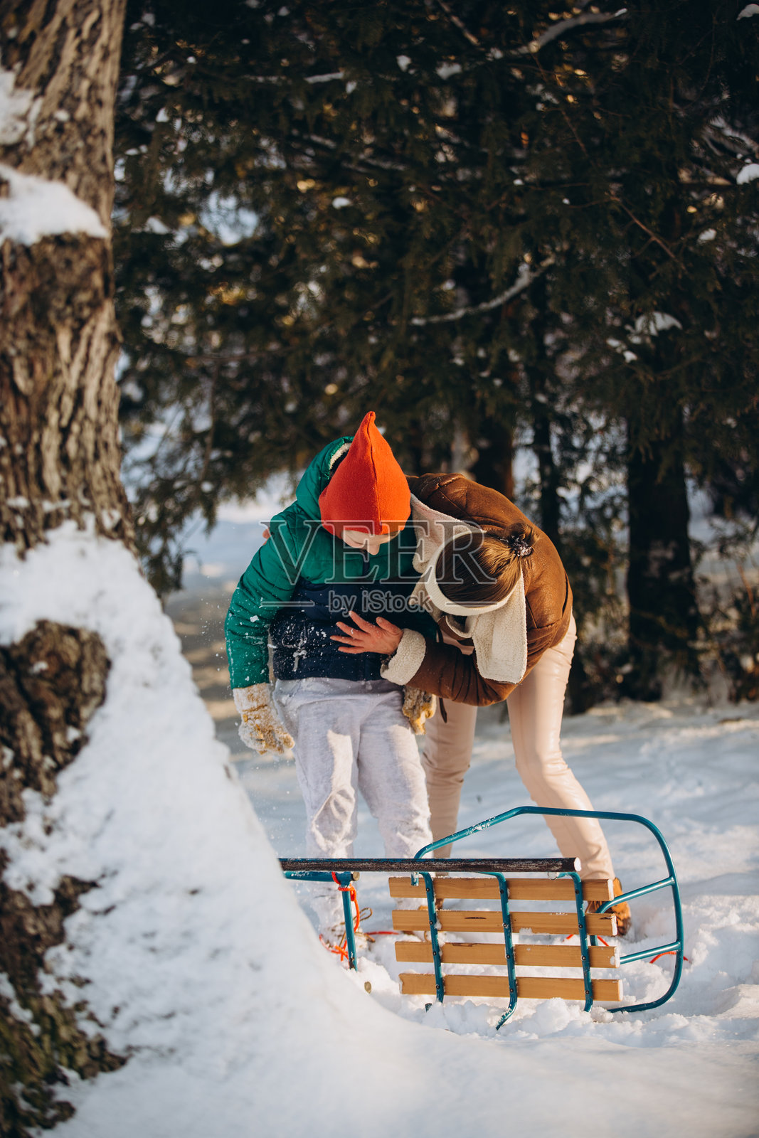妈妈在冬季公园协助儿子玩雪橇照片摄影图片