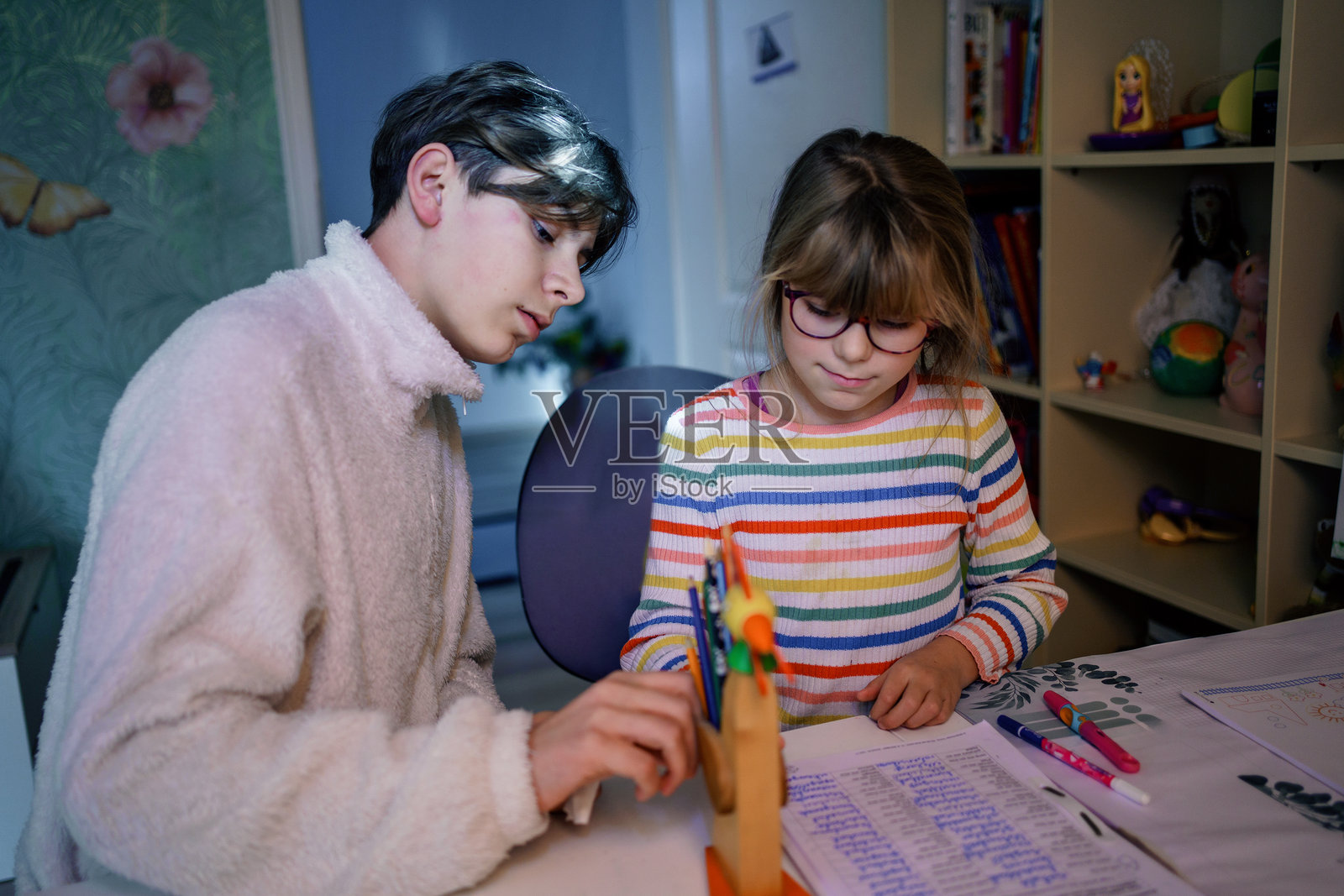 小女孩在房间里做作业，她看起来很沮丧。她的哥哥，一个十几岁的男孩，正在帮忙。照片摄影图片