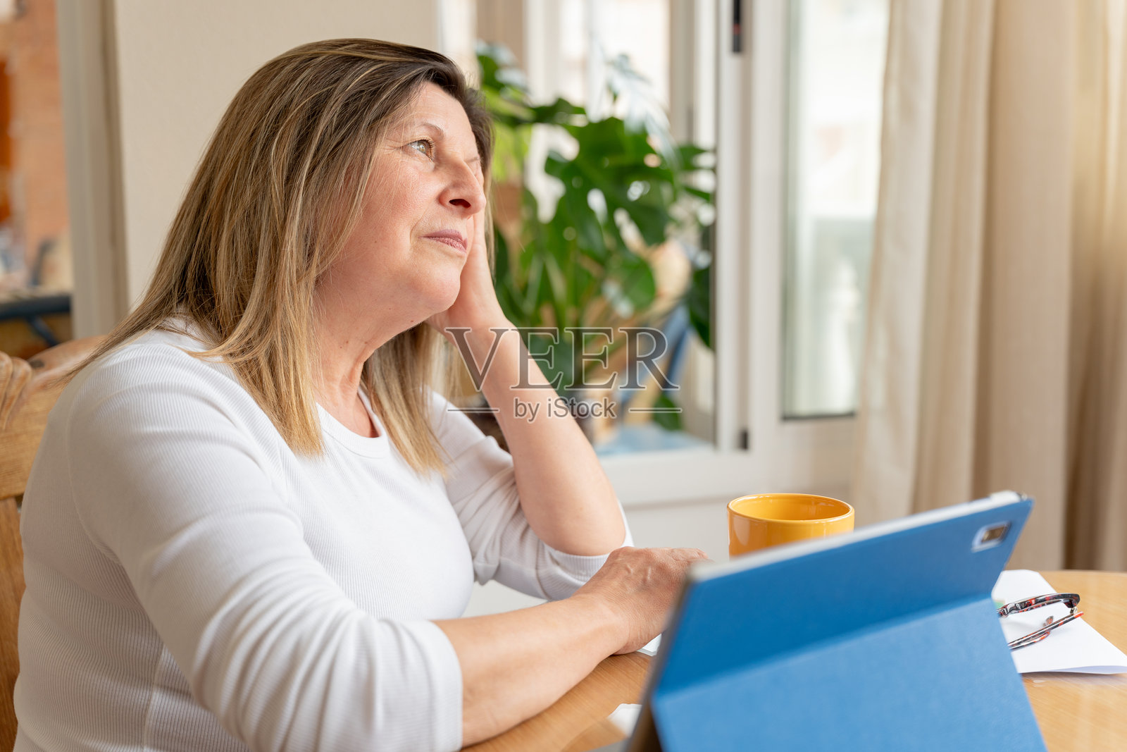 一位成熟的女性在家中望着远方，在操作数位平板电脑时陷入沉思照片摄影图片