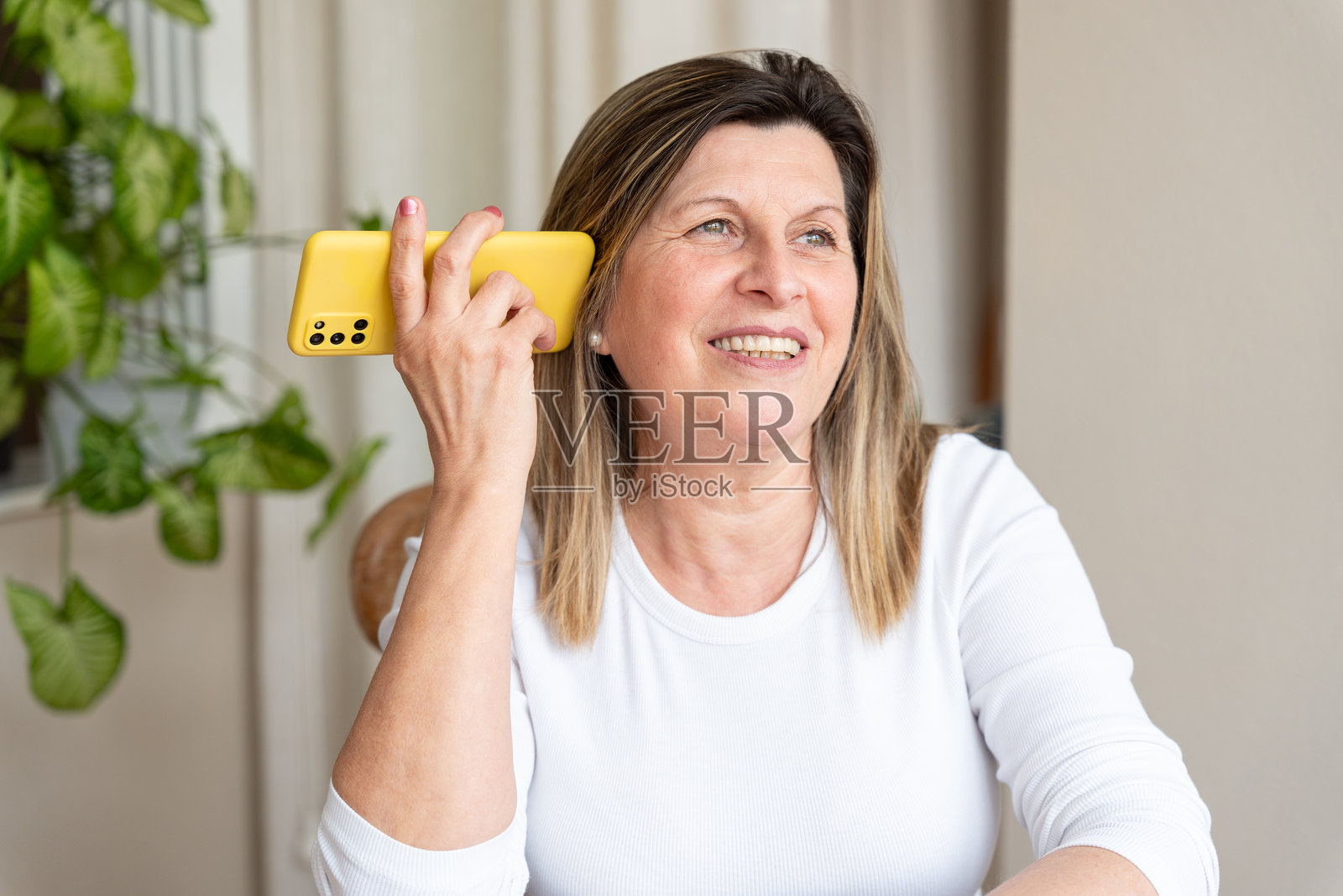 一位成熟的女士在家中愉快地用黄色智能手机交谈，享受沟通的乐趣照片摄影图片