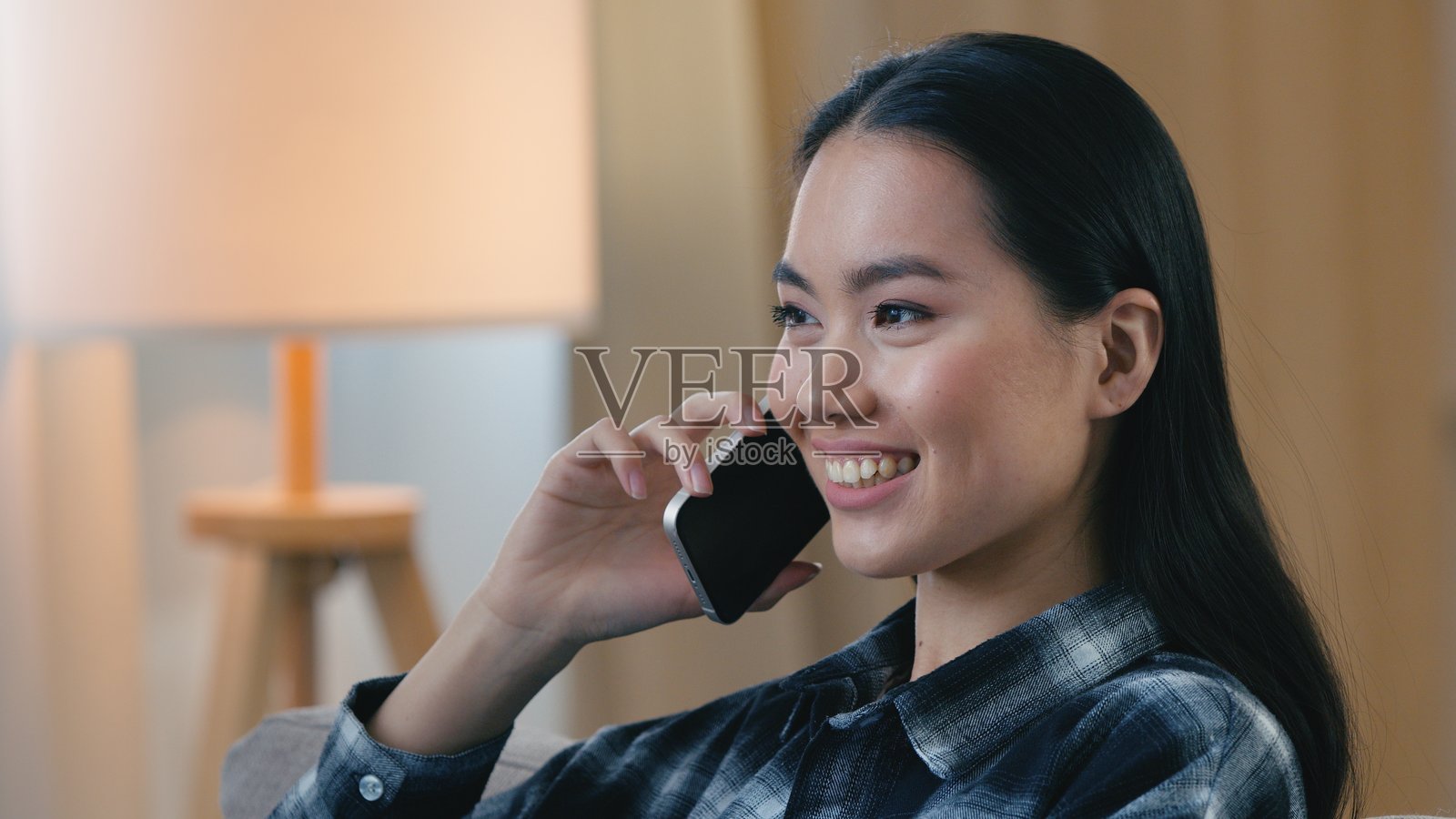 开心地笑着的亚洲女性在家中用手机交谈，友善微笑的女孩肖像在室内用智能手机聊天，韩裔、日裔、华裔女性正在远程讨论交流照片摄影图片