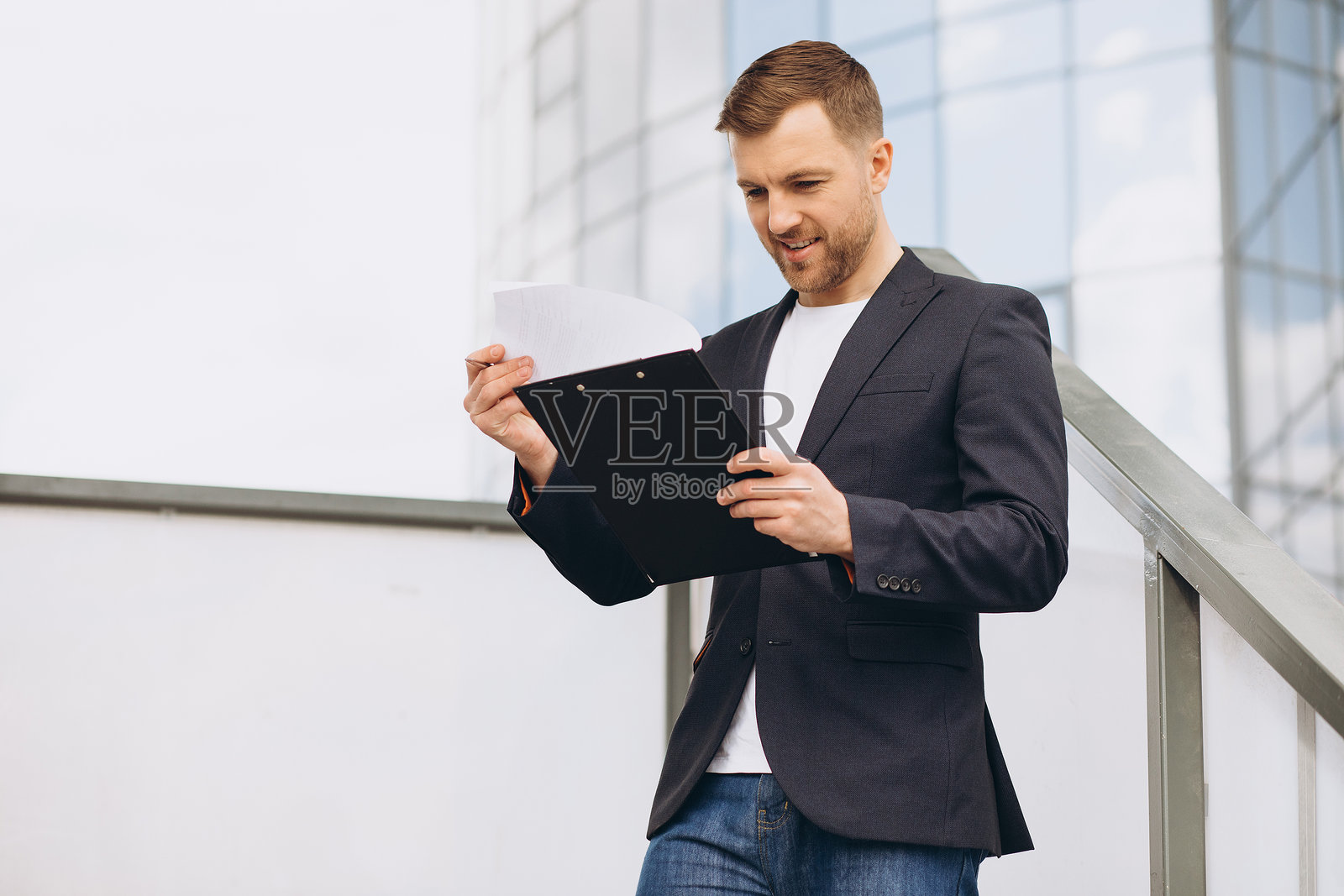 自信的商人在现代办公楼楼梯旁，在户外查看文件板上的文件照片摄影图片