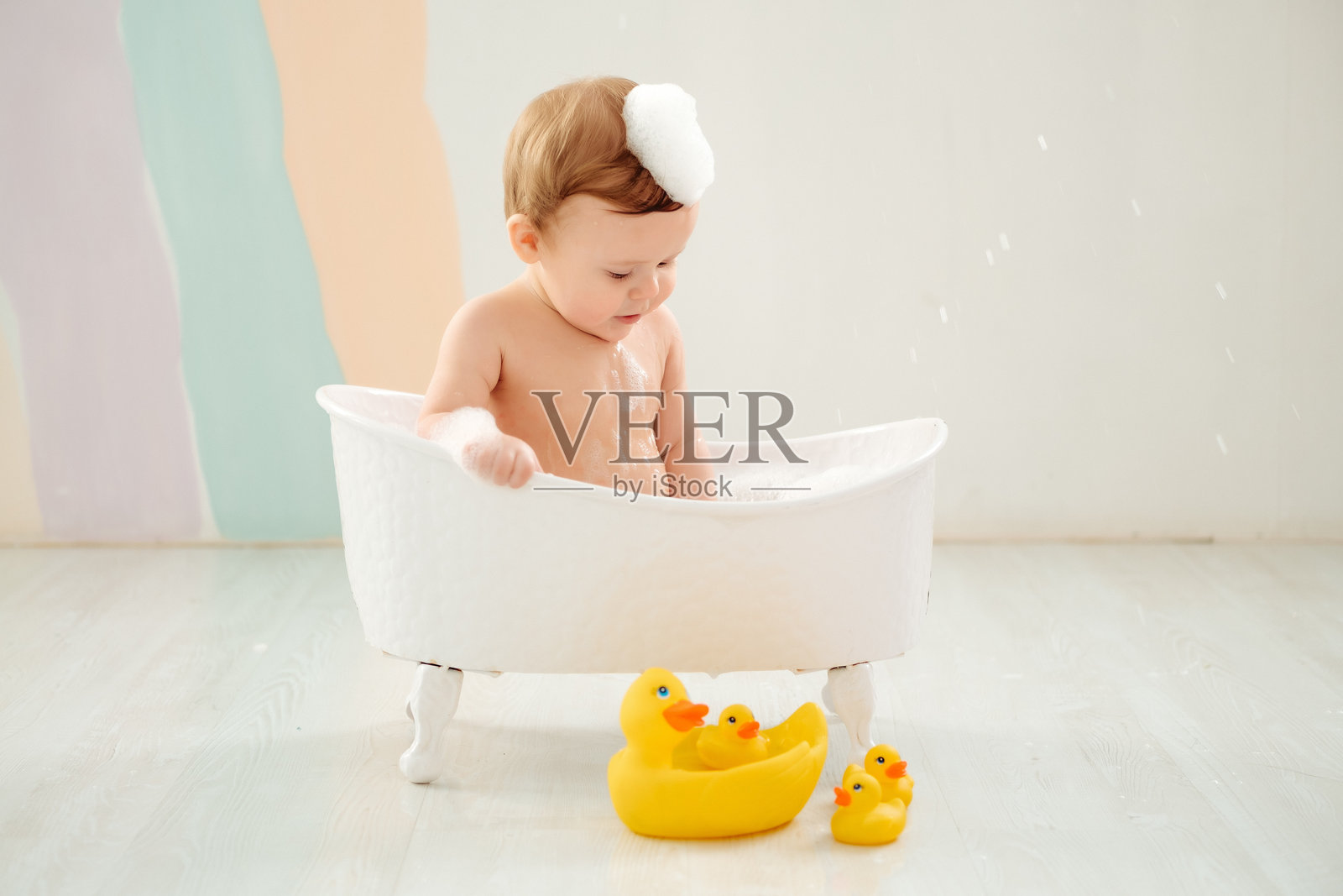 一个婴儿在浴缸里洗澡，周围有泡沫和橡皮鸭，体现了儿童卫生概念。一个小男孩在浴缸里玩耍或清洗，身上沾满了泡沫。照片摄影图片