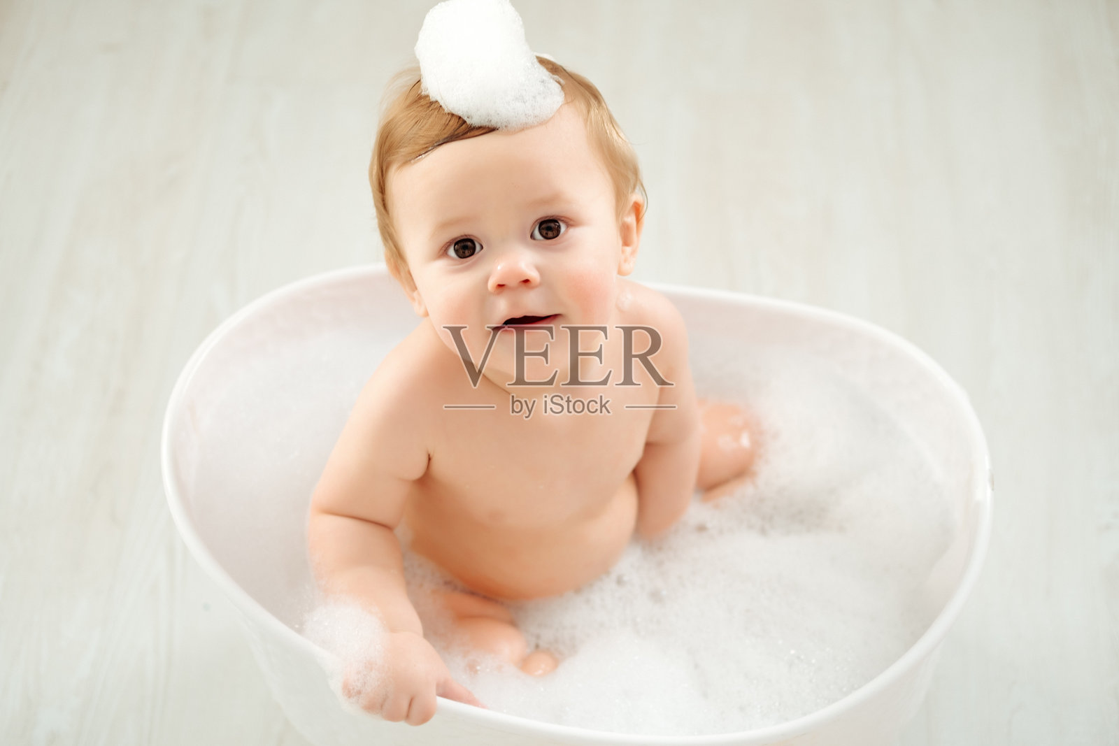 一个婴儿在浴缸里洗澡，周围有泡沫和橡皮鸭，体现了儿童卫生概念，一个小男孩在浴缸里玩耍或洗澡照片摄影图片