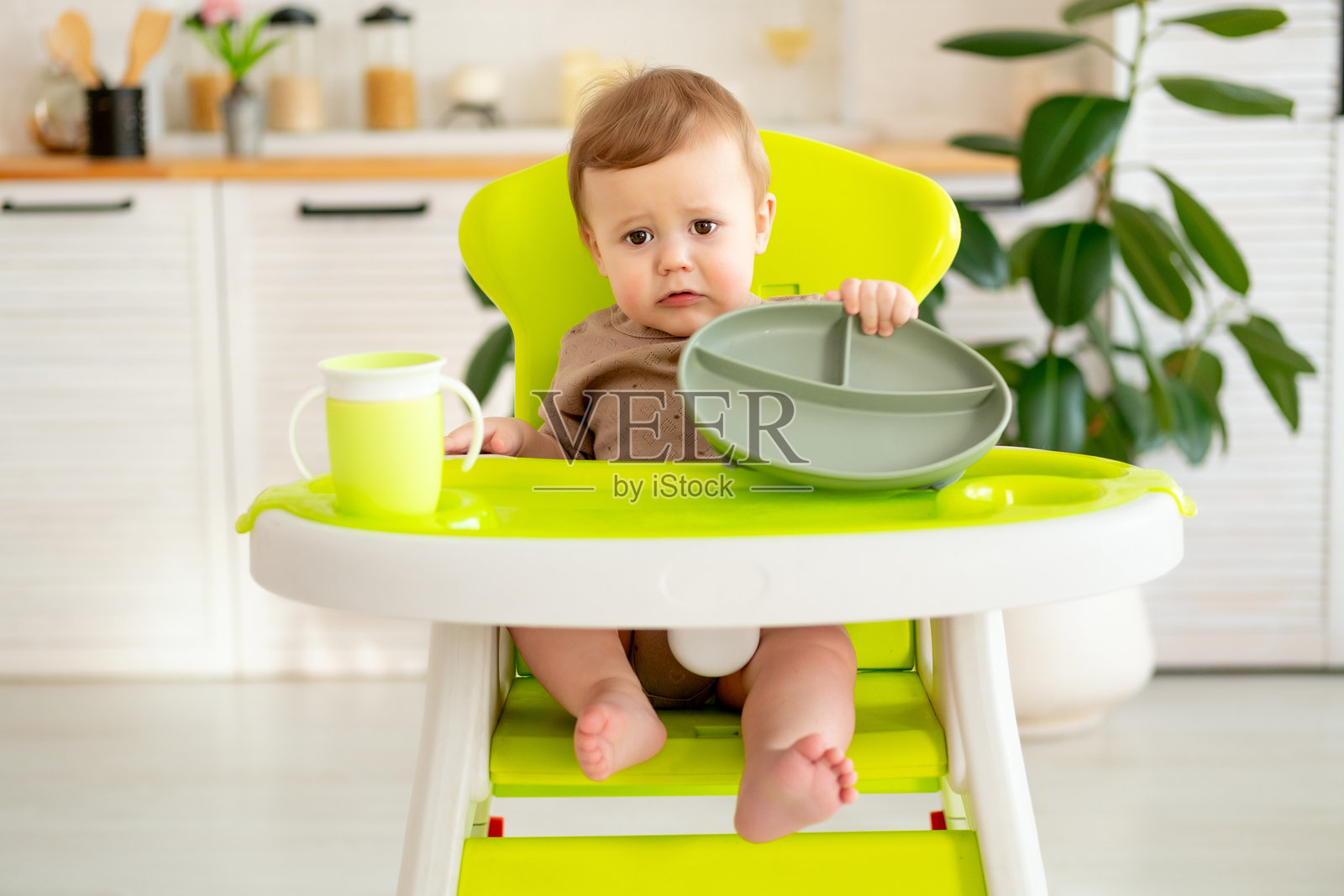 婴儿坐在高脚椅上吃水果，婴儿食品概念，孩子在厨房里喝水杯喝水照片摄影图片