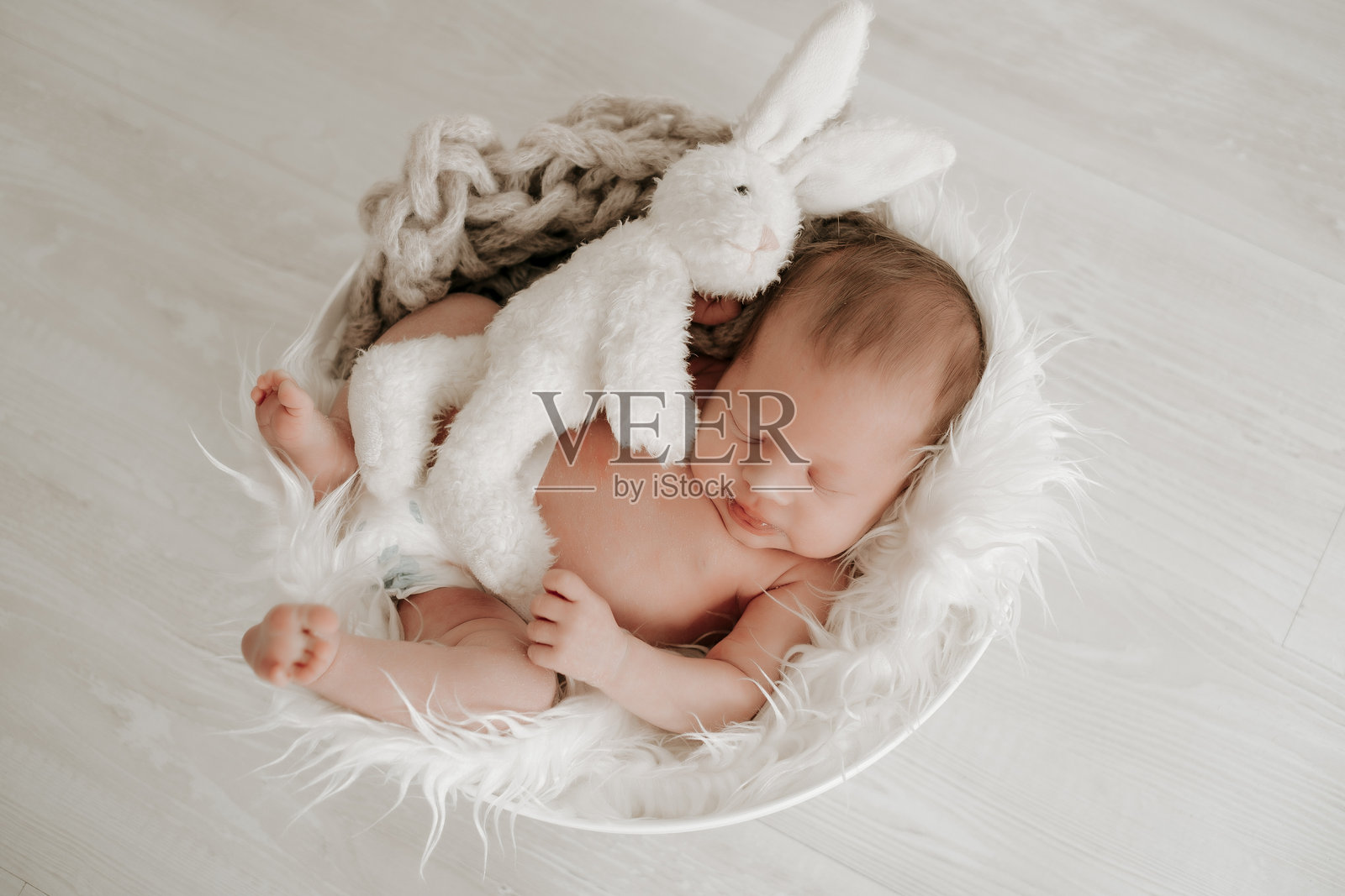一个婴儿和一个兔子睡在篮子里，一个新生儿安详地睡着，旁边有一个软毛玩具，留有文字空间照片摄影图片