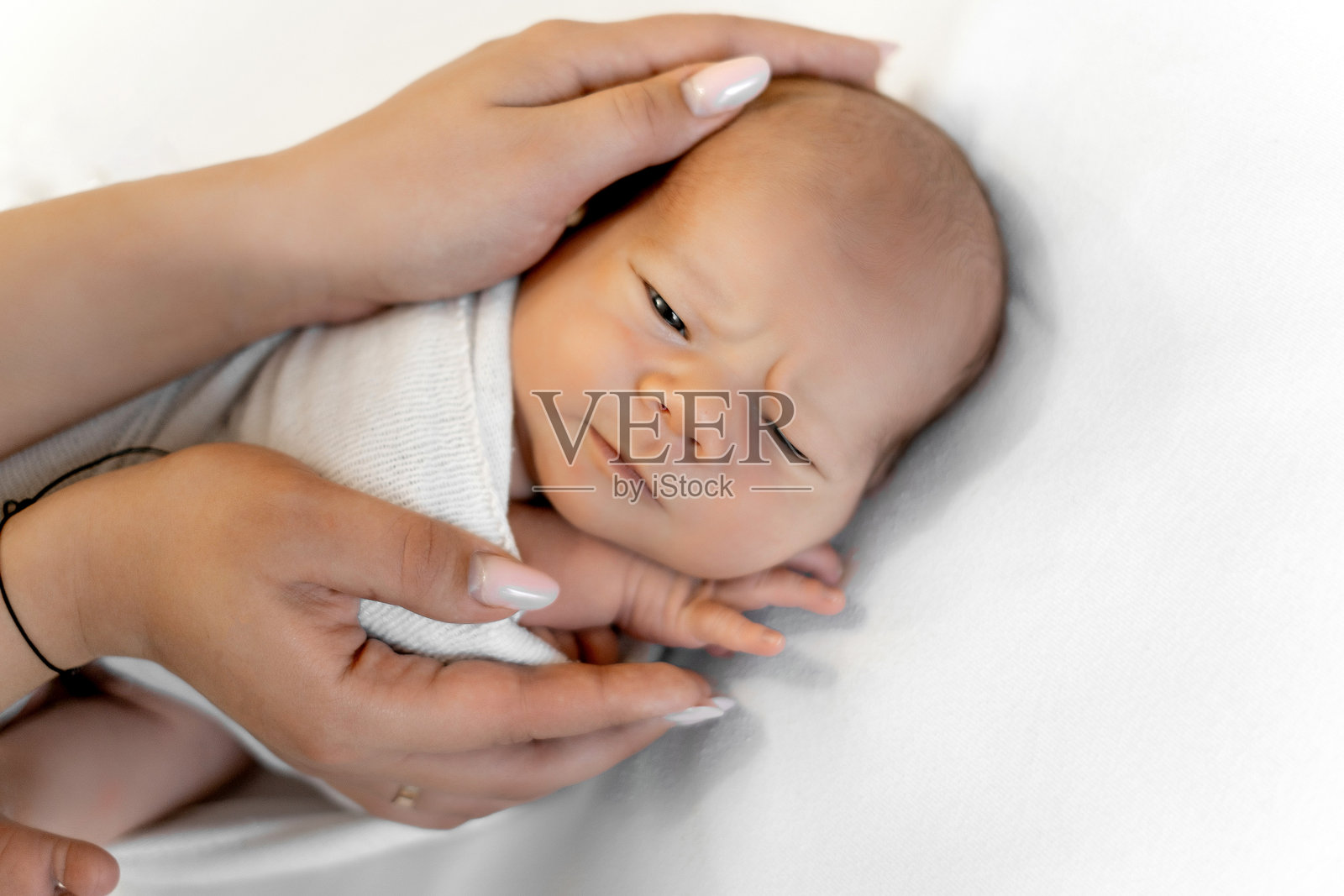 新生儿在白色背景下，安详地睡在母亲的怀抱中，婴儿熟睡，留有空白处可供添加文字照片摄影图片