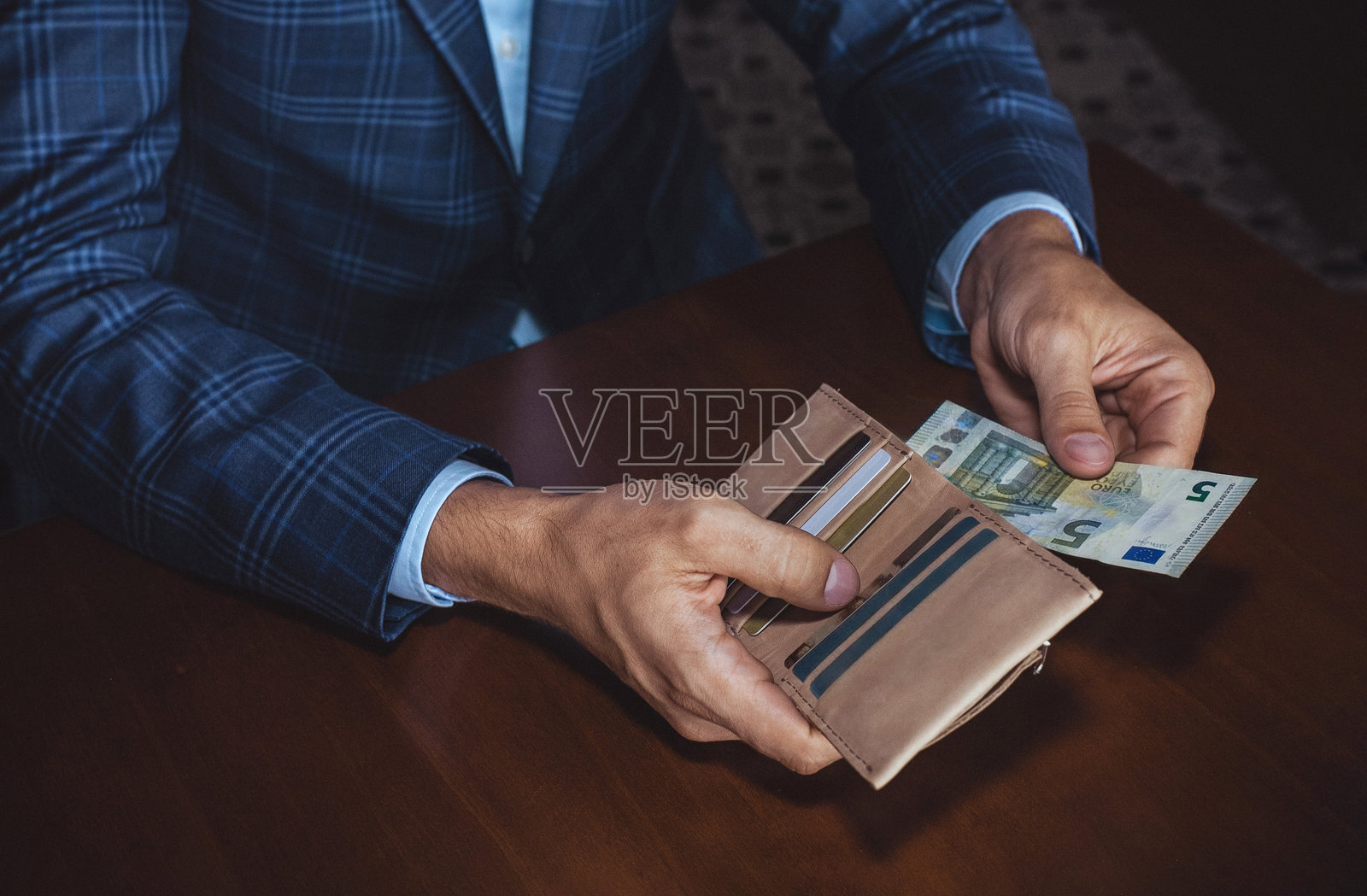 一位穿着格子西装的男士手持钱包和现金，在带有木桌的时尚室内环境中展示金融交易。照片摄影图片