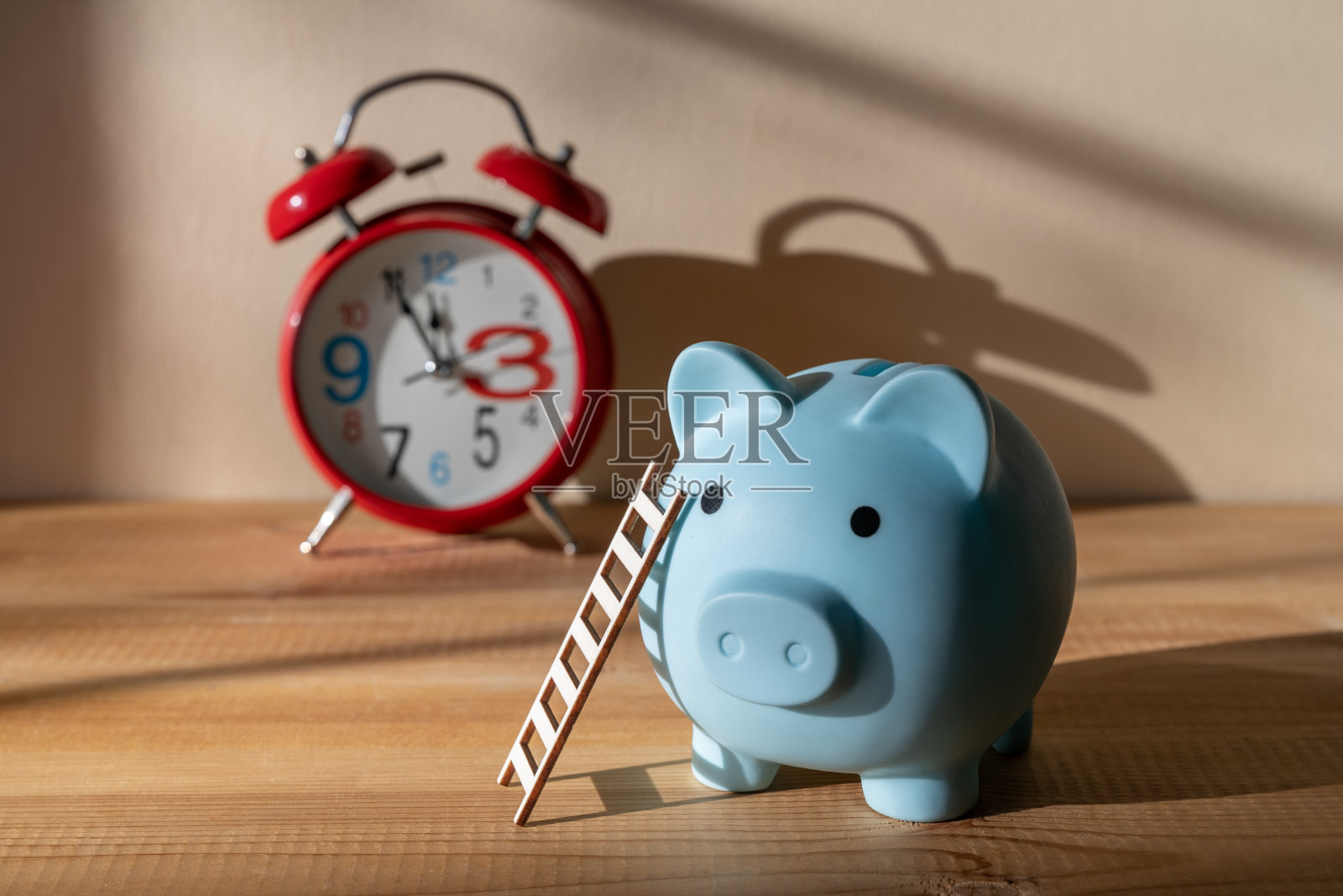 墙边放着一个存钱罐，旁边有梯子和红色闹钟，并投下阴影照片摄影图片