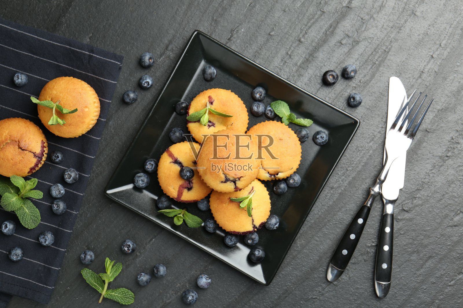 美味的蓝莓玛芬，配有薄荷和餐具，放在深色纹理桌上，俯视角度照片摄影图片