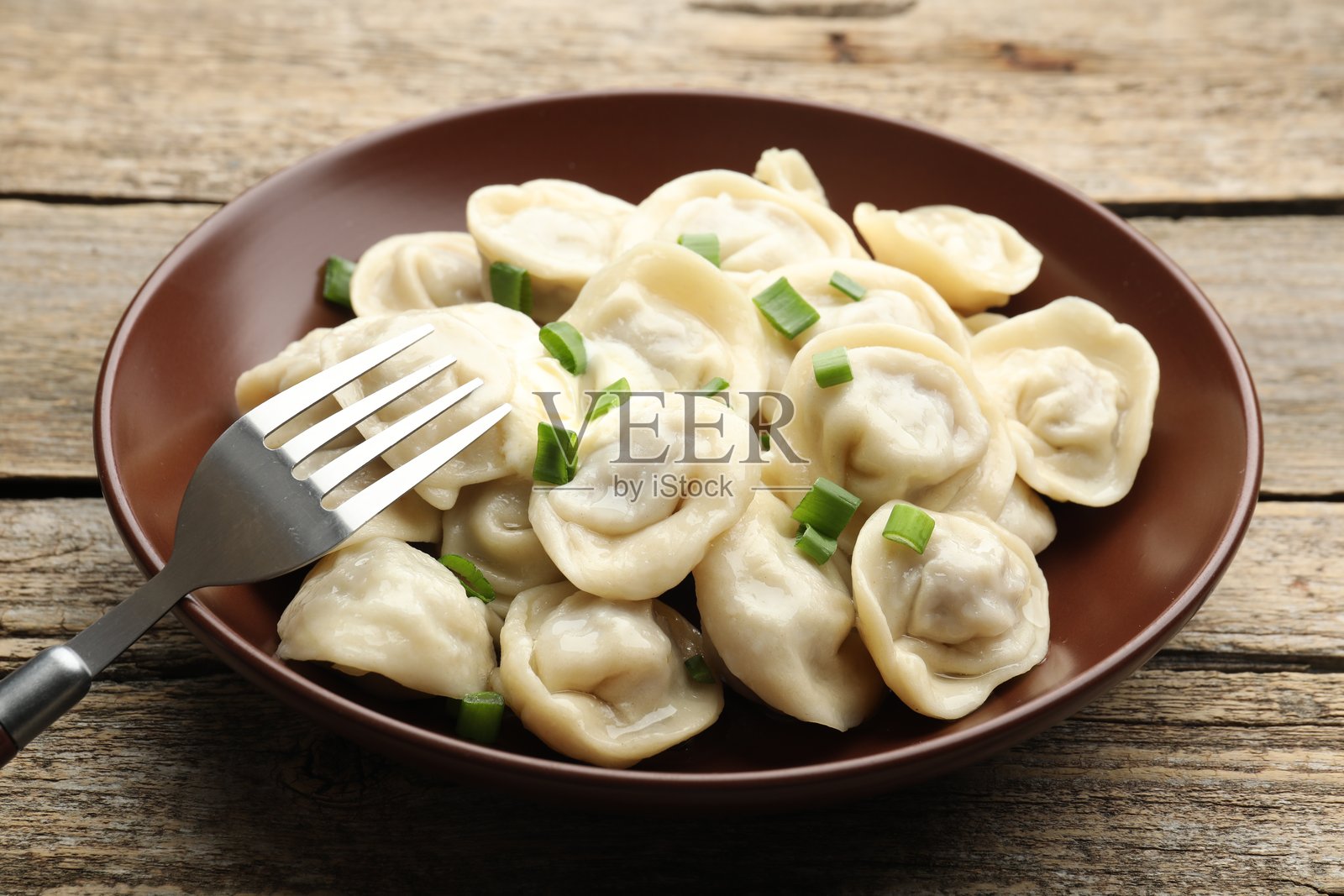 木桌上美味的饺子，配有葱花和叉子，特写照片摄影图片