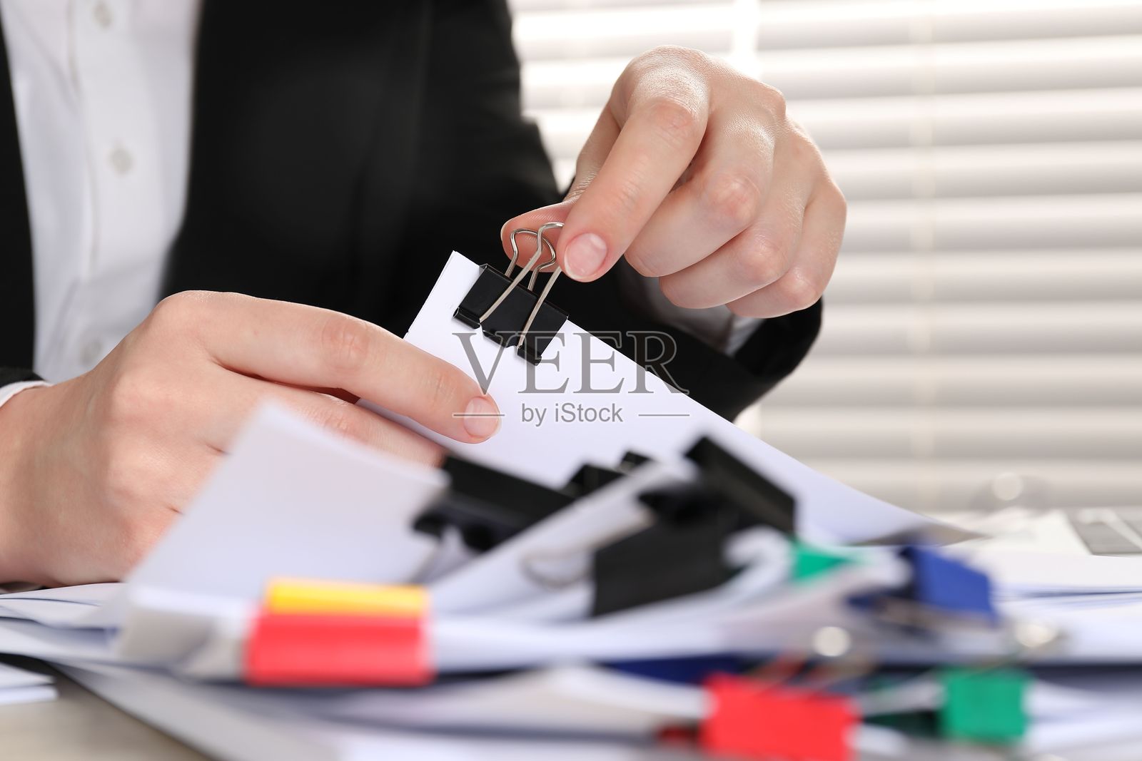 女子在桌上用金属长尾夹装订纸张，特写照片摄影图片