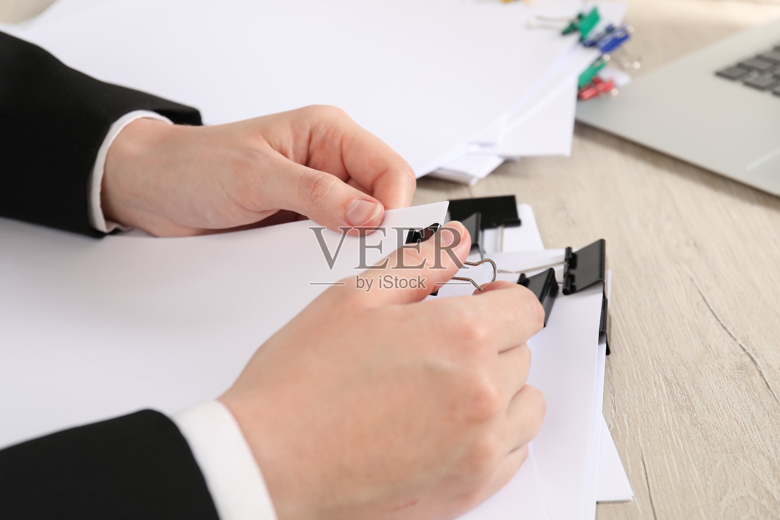 女子在木桌上用金属夹子固定纸张，特写照片摄影图片