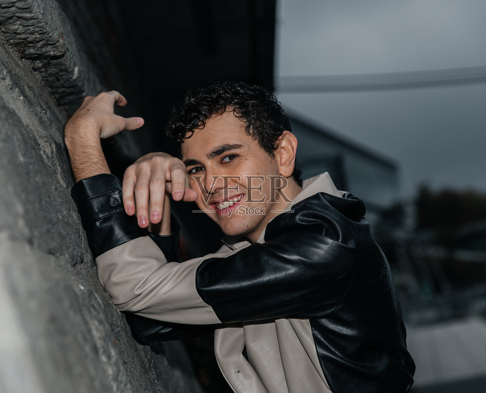 穿着时尚夹克的年轻西班牙裔男性在城市环境中微笑照片摄影图片