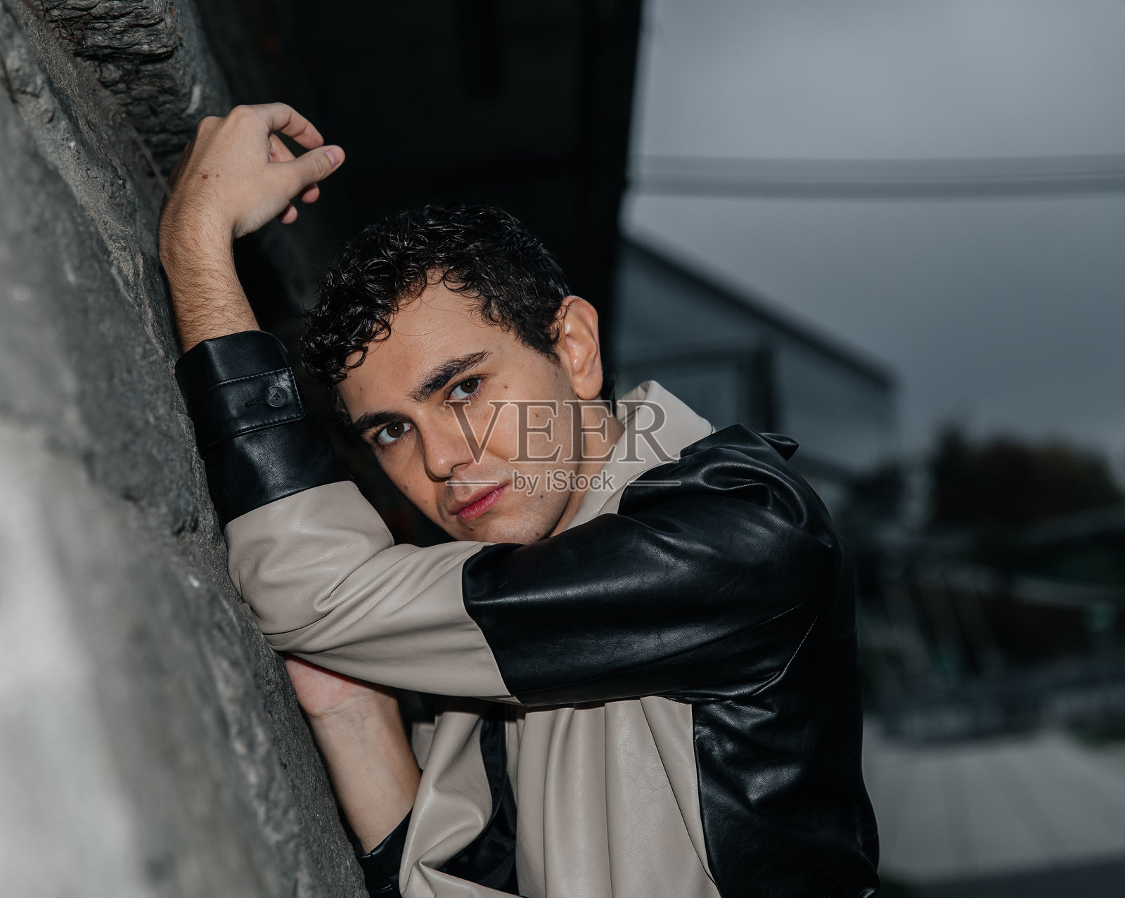 穿着风衣的年轻白人男性靠墙而立在户外照片摄影图片