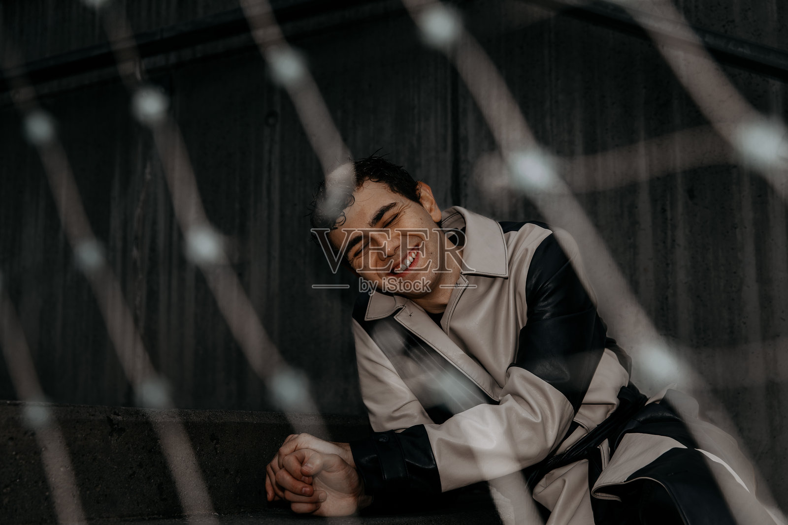 身穿时尚外套的年轻西班牙裔男性，透过网格看向镜头并微笑照片摄影图片