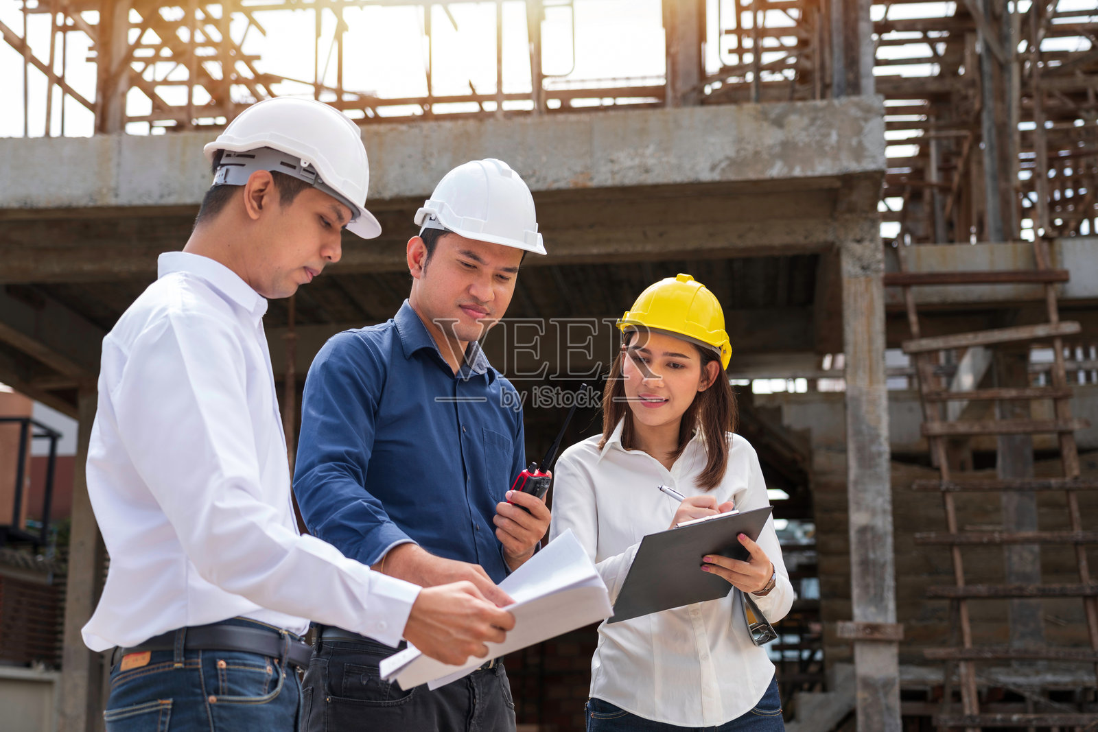 工程师团队与工人在现场开会讨论建筑蓝图，并指向工地工作场所。身戴安全帽的建筑工人和建筑师在建筑工地上查看蓝图。照片摄影图片