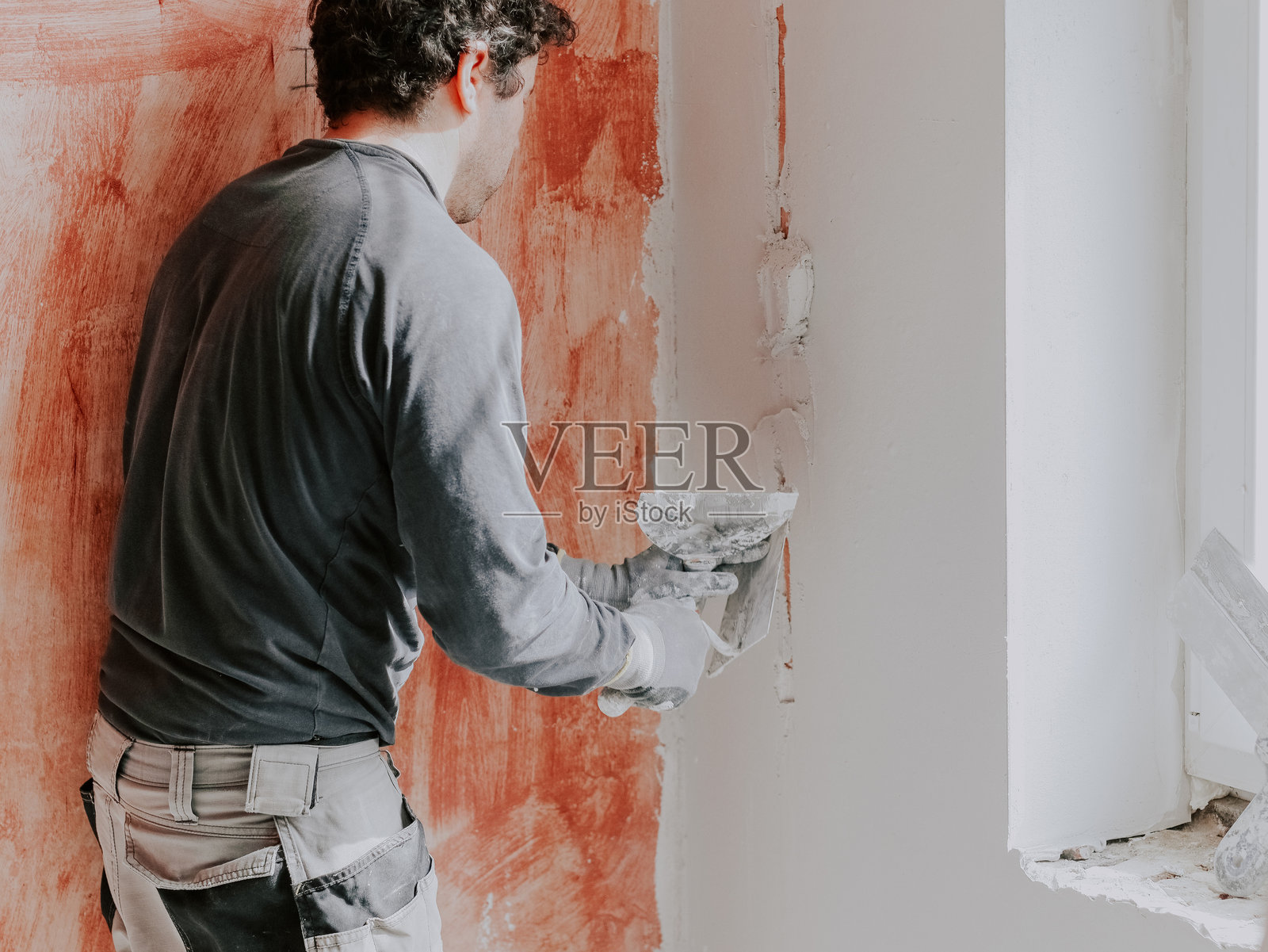 一位高加索年轻男子正在给墙壁刮腻子。照片摄影图片