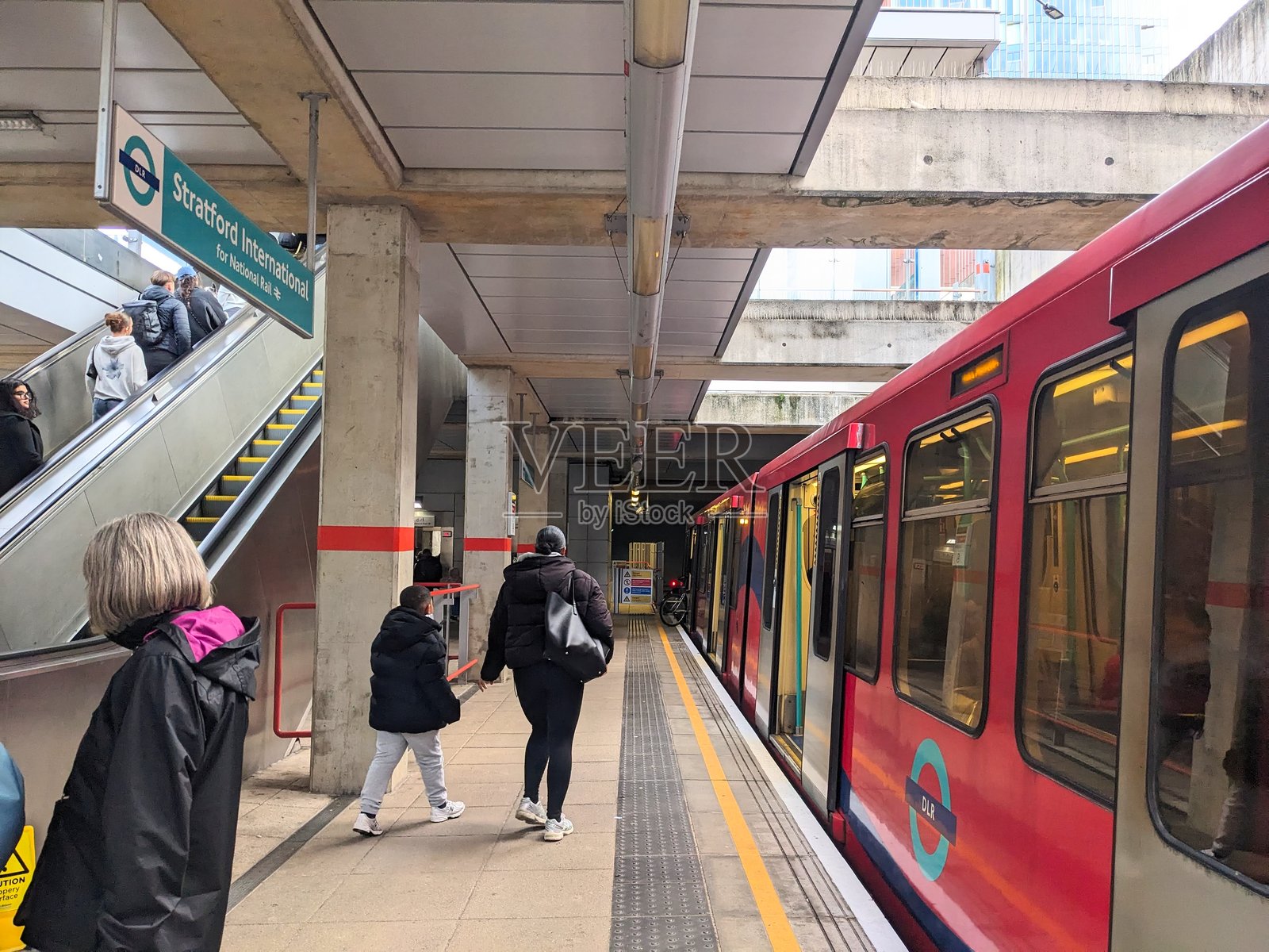 红色DLR列车停靠在斯特拉特福德国际站，站台上可以看到乘客和自动扶梯。照片摄影图片