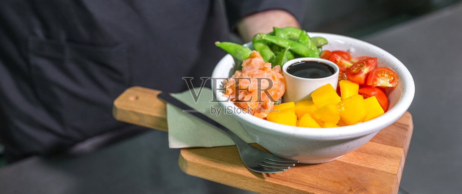 餐厅厨房里，一位身份不明的厨师展示着色彩鲜艳、装有三文鱼的生鱼饭特写照片摄影图片