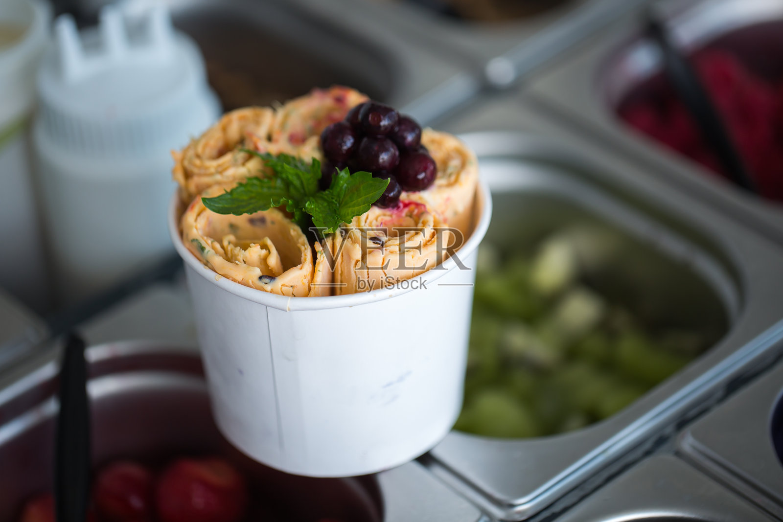 在冷冻锅里制作的炒冰卷。卷式冰淇淋，手工制作的冰淇淋甜点。带钢制冷冻盘的炒冰机。照片摄影图片