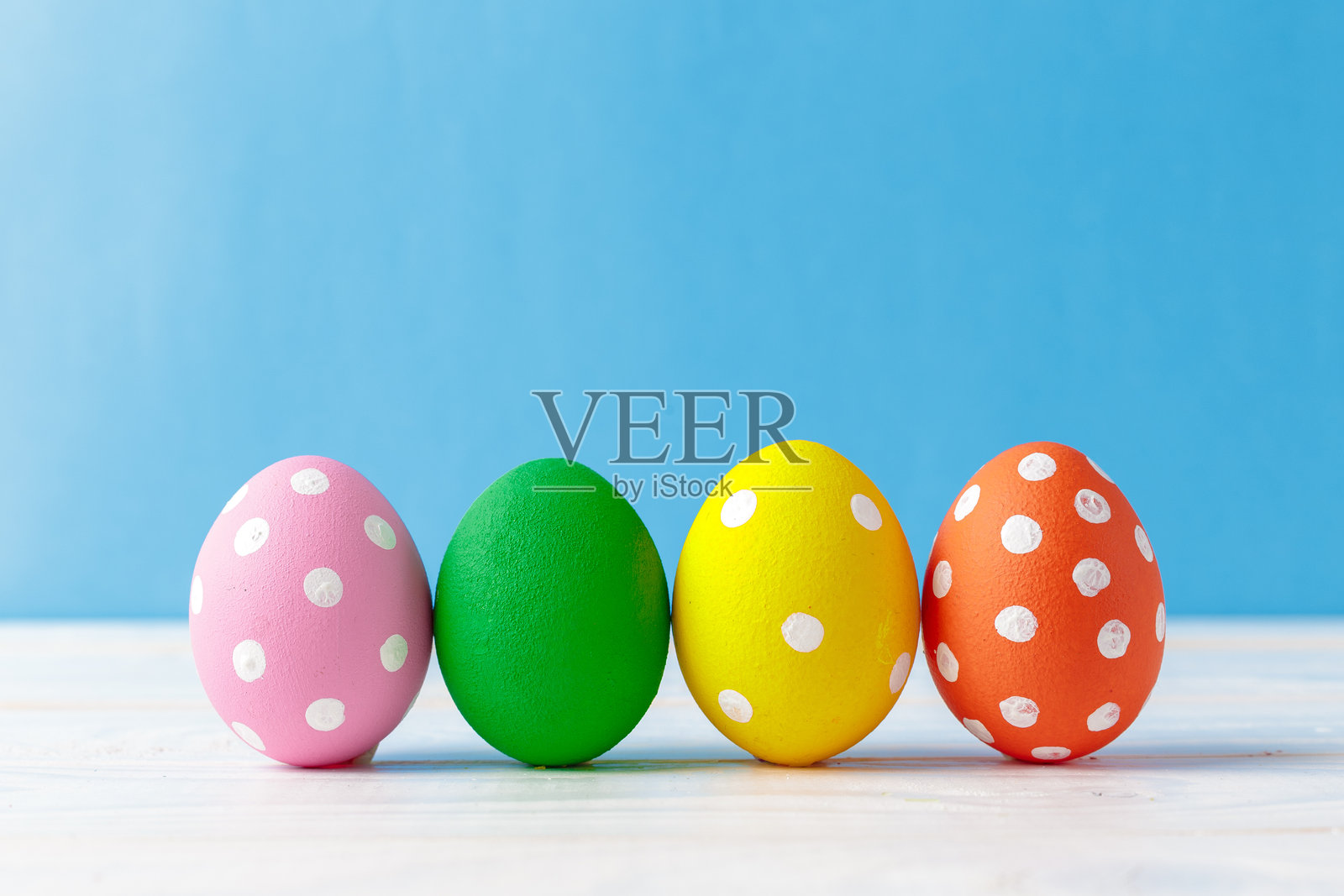 蓝底背景下的餐桌上摆放着彩色的波点鸡蛋照片摄影图片