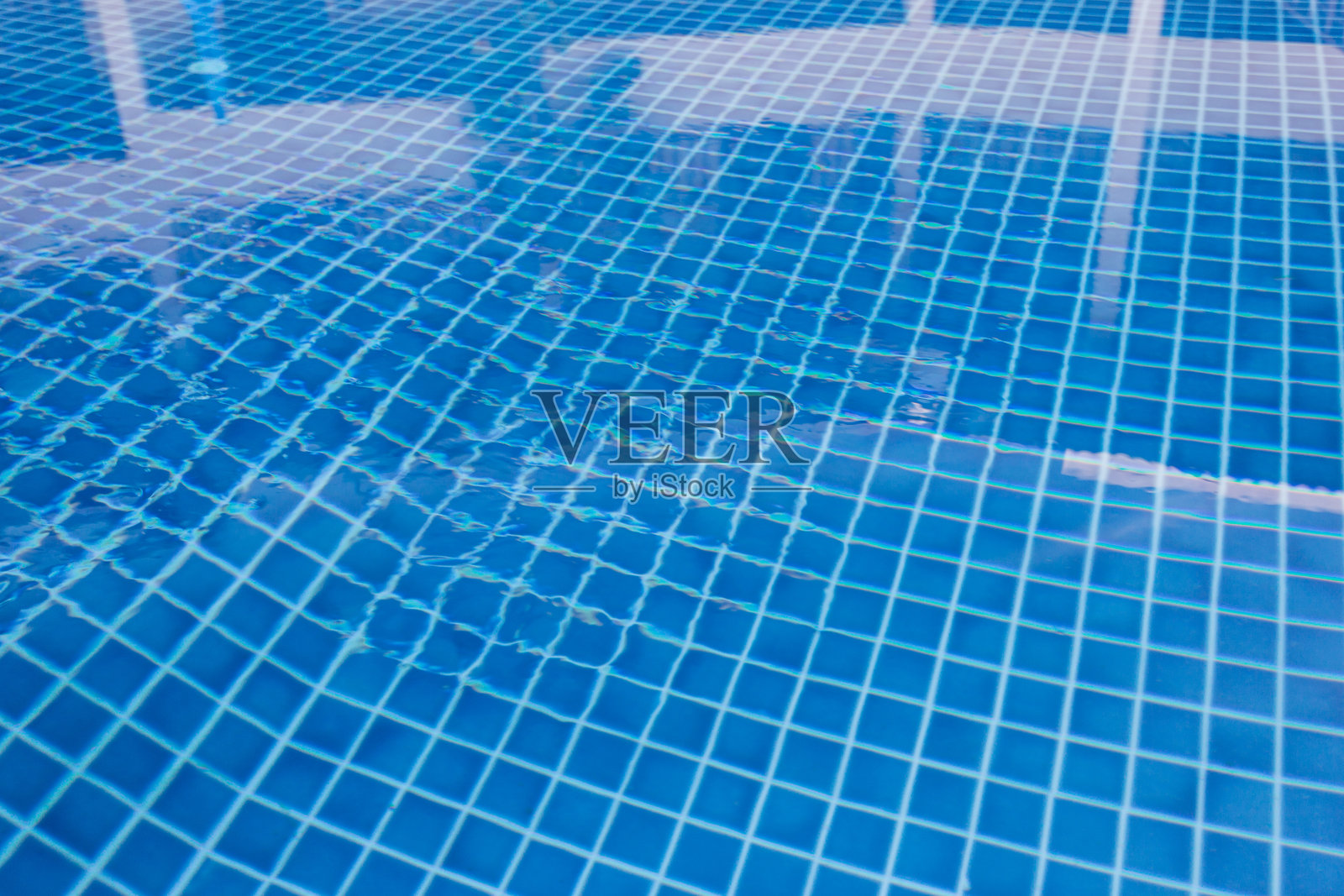 阳光明媚的日子里，游泳池的蓝色瓷砖水面照片摄影图片