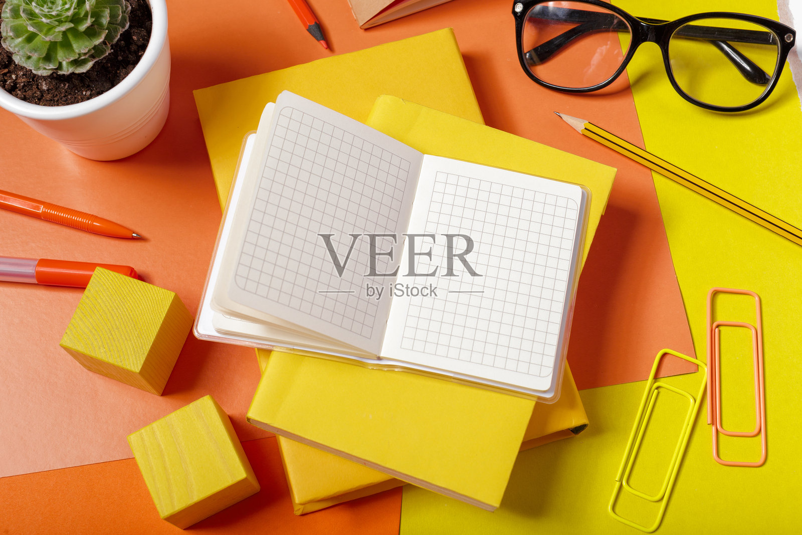 色彩鲜艳的桌子上摆放着笔记本、钢笔和一盆植物的工作区照片摄影图片