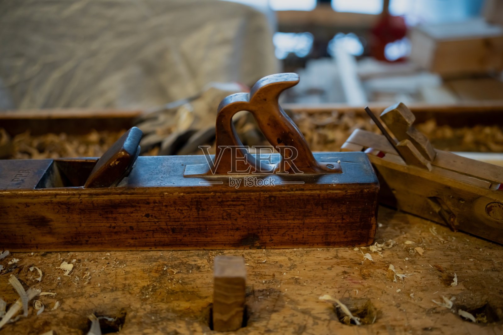 老式木工手刨放在粗糙的木桌上，上面有木屑和刨花，背景是手工木艺工具的乡村工坊内部照片摄影图片