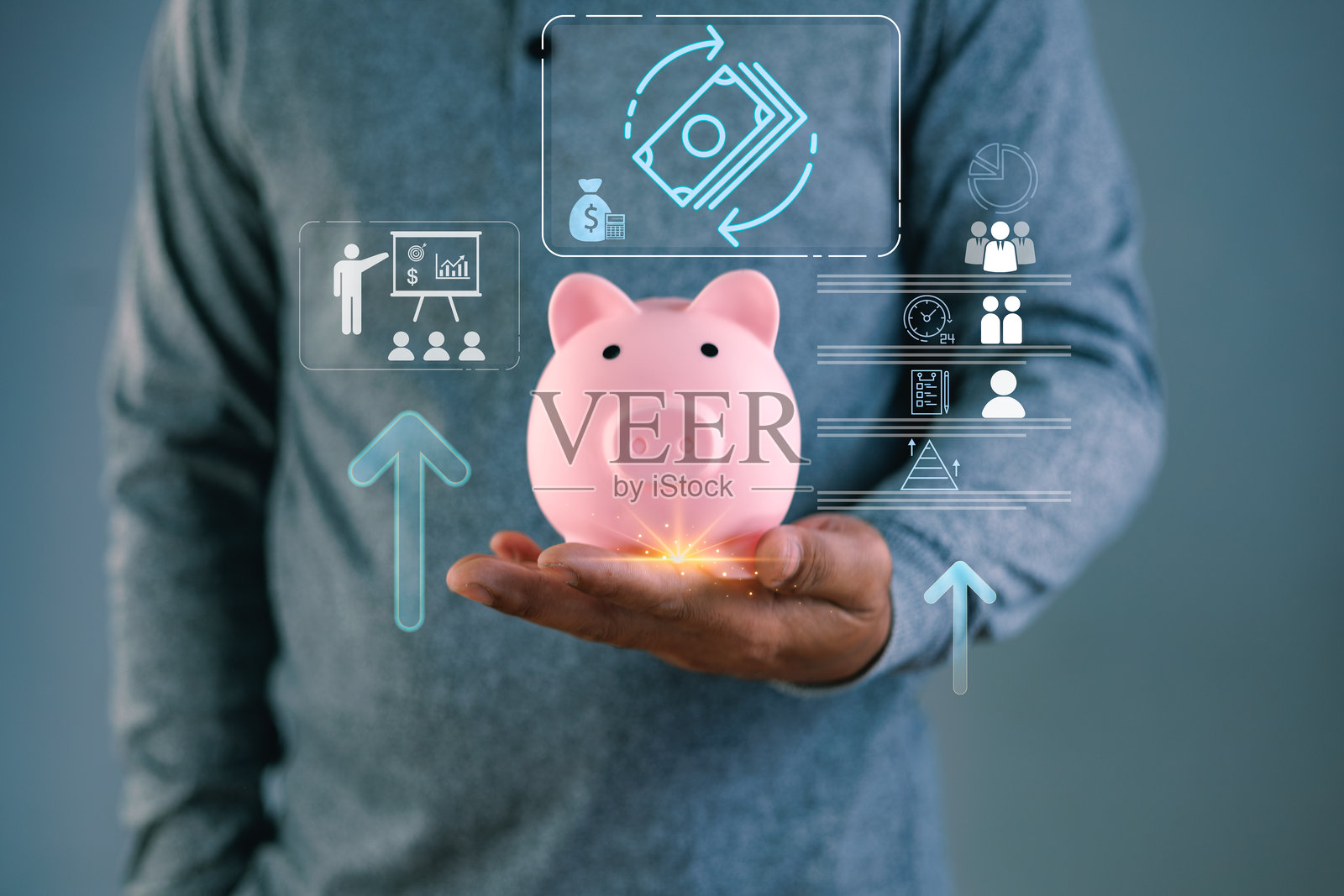 商人手持粉色储蓄罐，周围环绕着虚拟的金融增长图标和资金管理界面。体现了储蓄概念、财富投资策略以及成功的商业银行规划。照片摄影图片