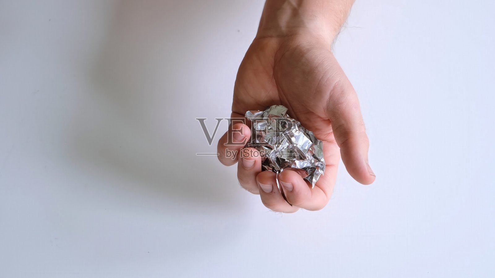 特写镜头俯视男性双手在白色背景上揉搓锡纸。概念是“小题大做”或“问题的本质”。表面上的大与现实的对比。高质量照片照片摄影图片