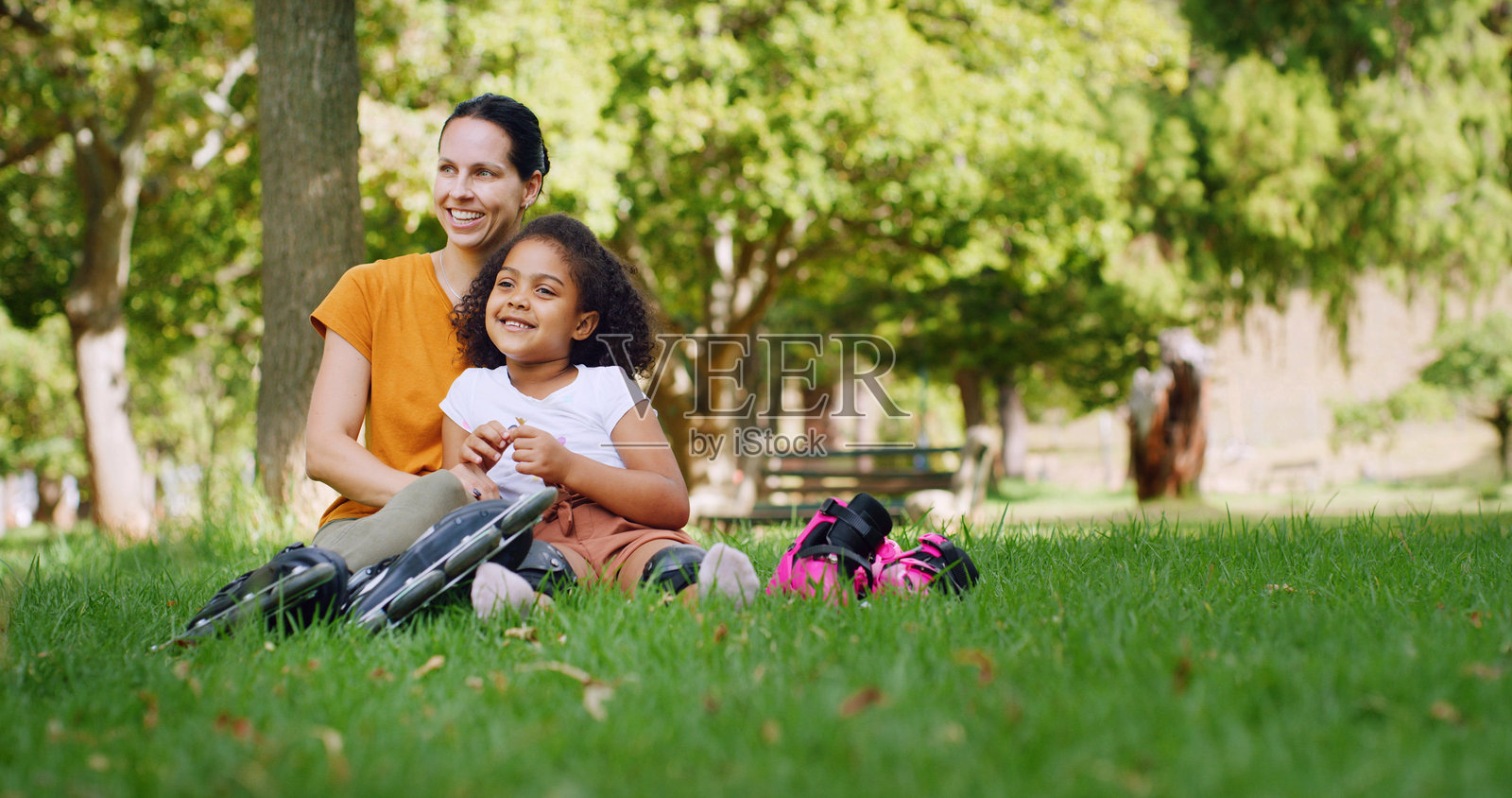 公园里，一位母亲和女儿在玩轮滑，享受轻松愉快的时光，面带笑容，如同进行一场溜冰游戏。在自然环境中，这位女士和孩子在夏日假期里享受轮滑的乐趣，享受亲子时光、爱好和家庭度假的幸福。照片摄影图片